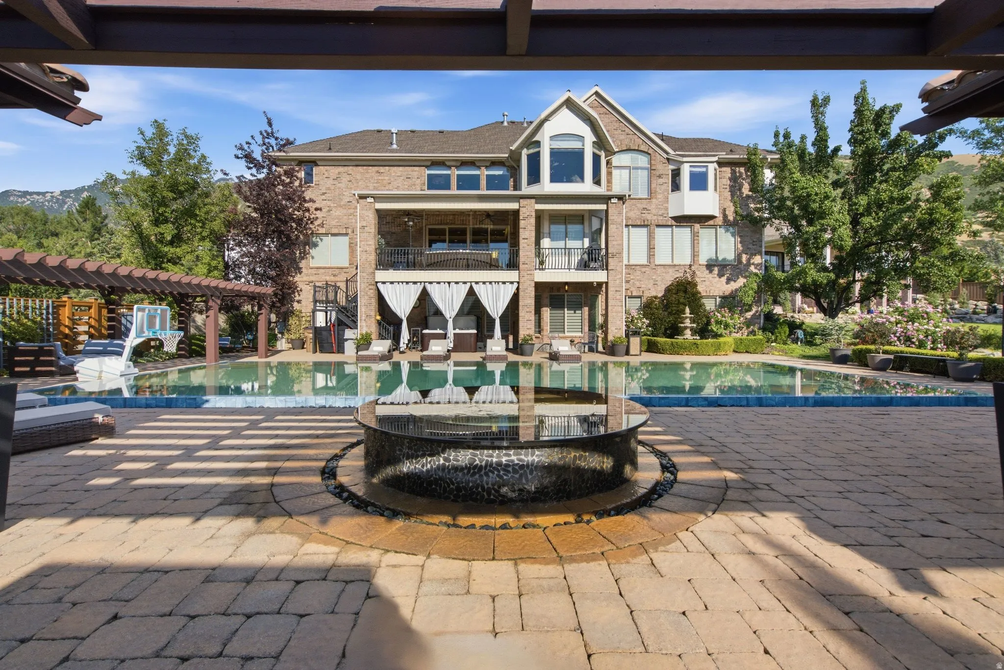 Expansive paver patio with a circular fire feature, leading to a large swimming pool