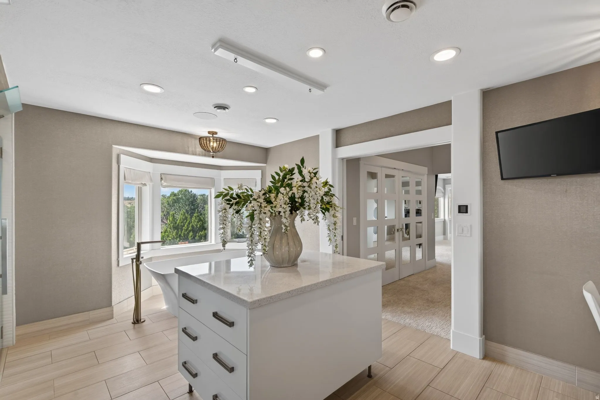 Freestanding bathtub with floor-mounted faucet, bay window, white cabinetry with stone countertop, tile flooring, and recessed lighting