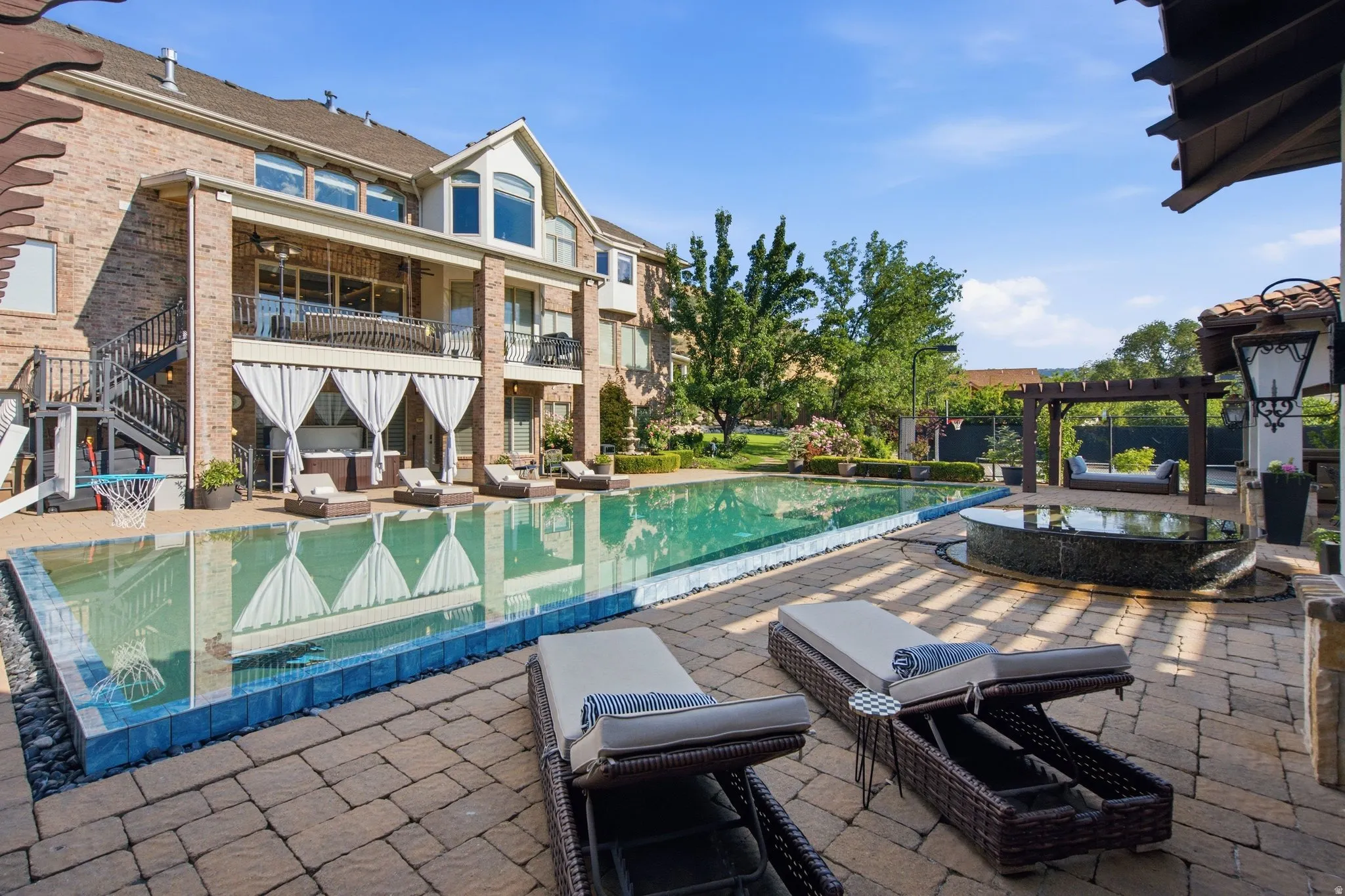 Extensive paver patio with a rectangular swimming pool, integrated hot tub, and a pergola-covered lounge area