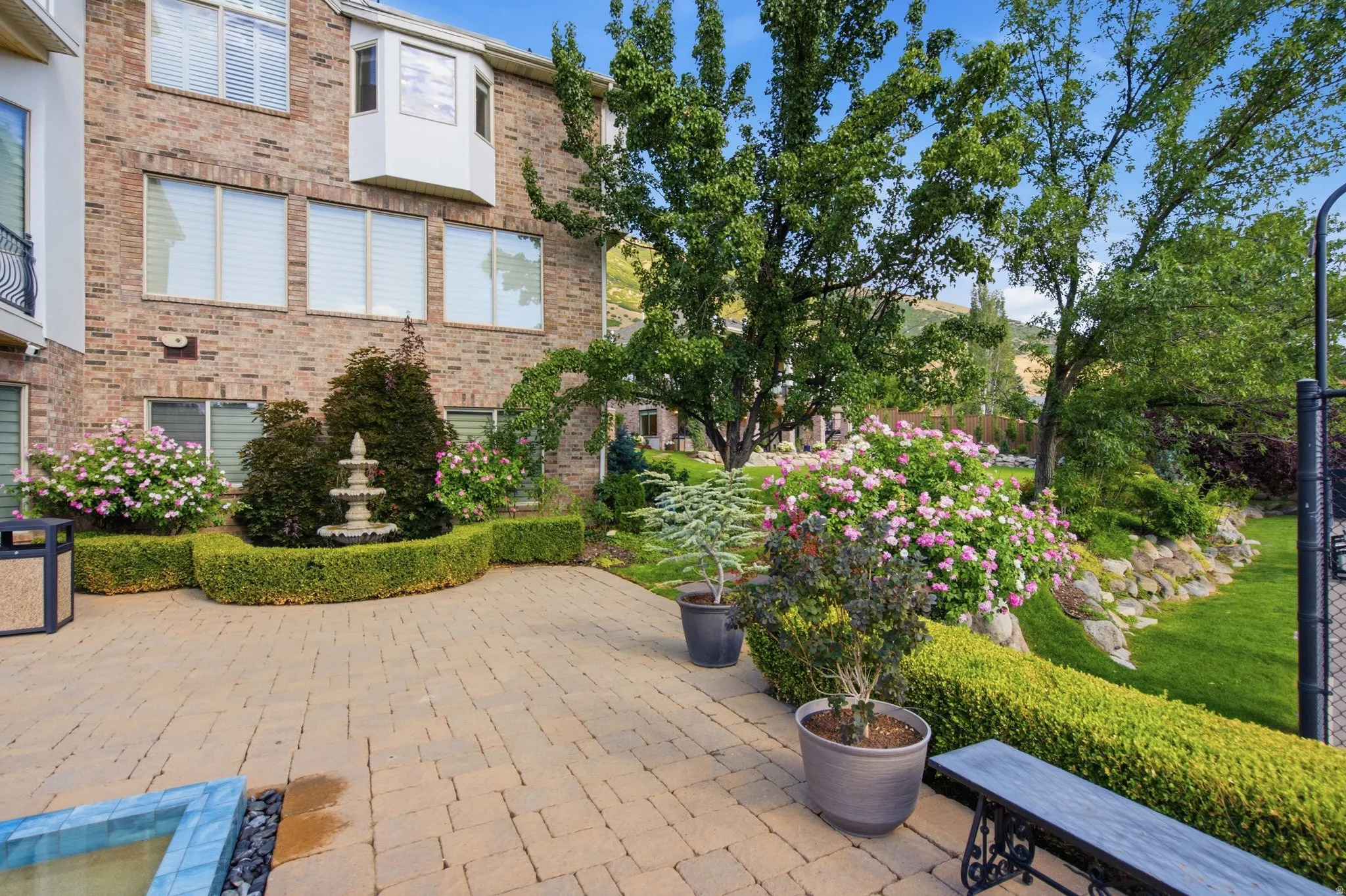 Brick exterior with multiple windows, paver patio, stone fountain, and mature landscaping
