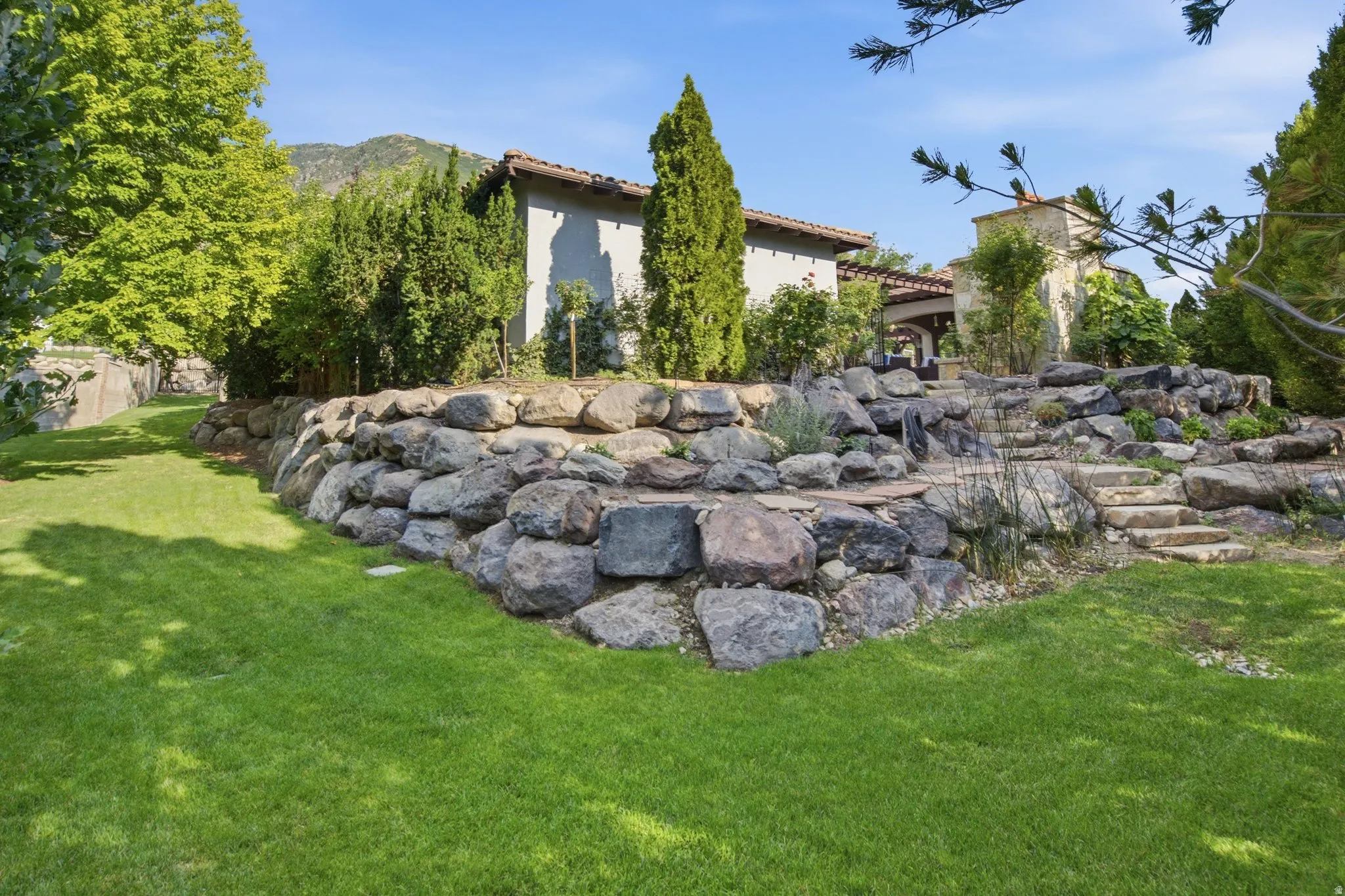 Expansive lawn with a natural stone retaining wall, terraced landscaping, and stone steps
