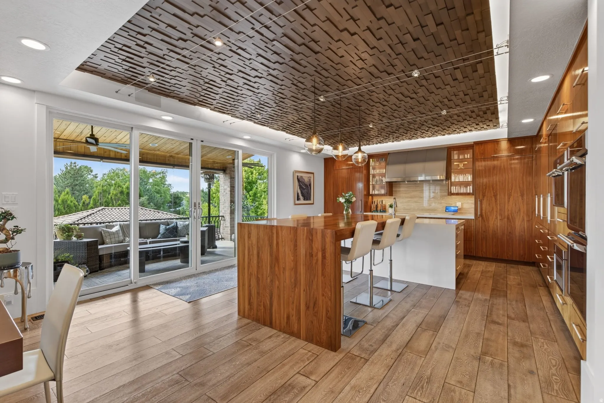 Wood-finish flooring, full-height paneled cabinetry, kitchen island with integrated seating, stainless steel appliances, and a wood-paneled ceiling feature