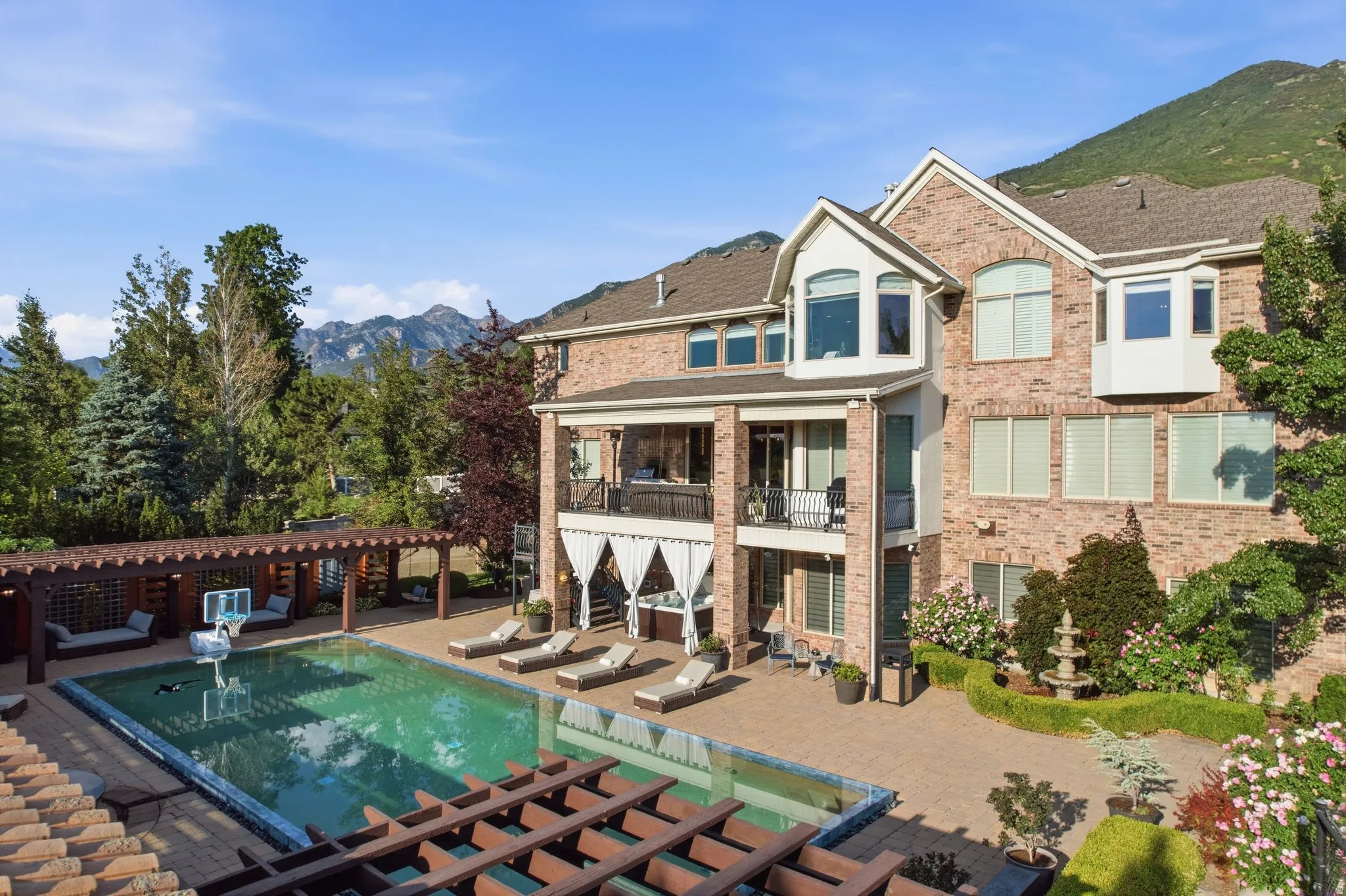 Brick exterior architecture with multiple windows, an outdoor swimming pool, and an extensive paver patio