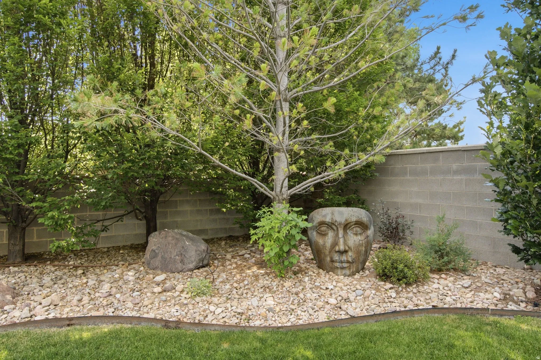 Landscaped garden bed featuring mature trees, decorative rock, a large boulder, and a unique garden sculpture
