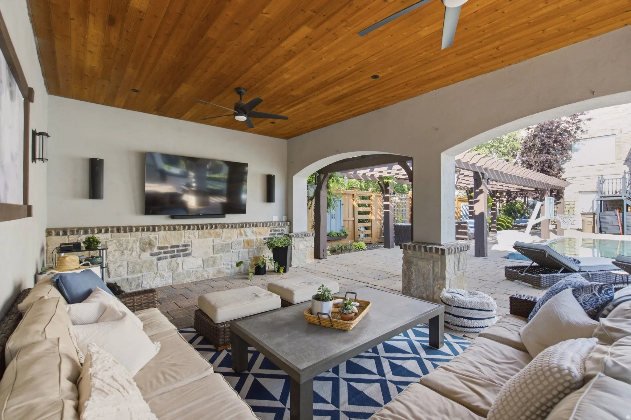 Covered outdoor living area with wood-finish ceiling, ceiling fans, and stone-finish wall
