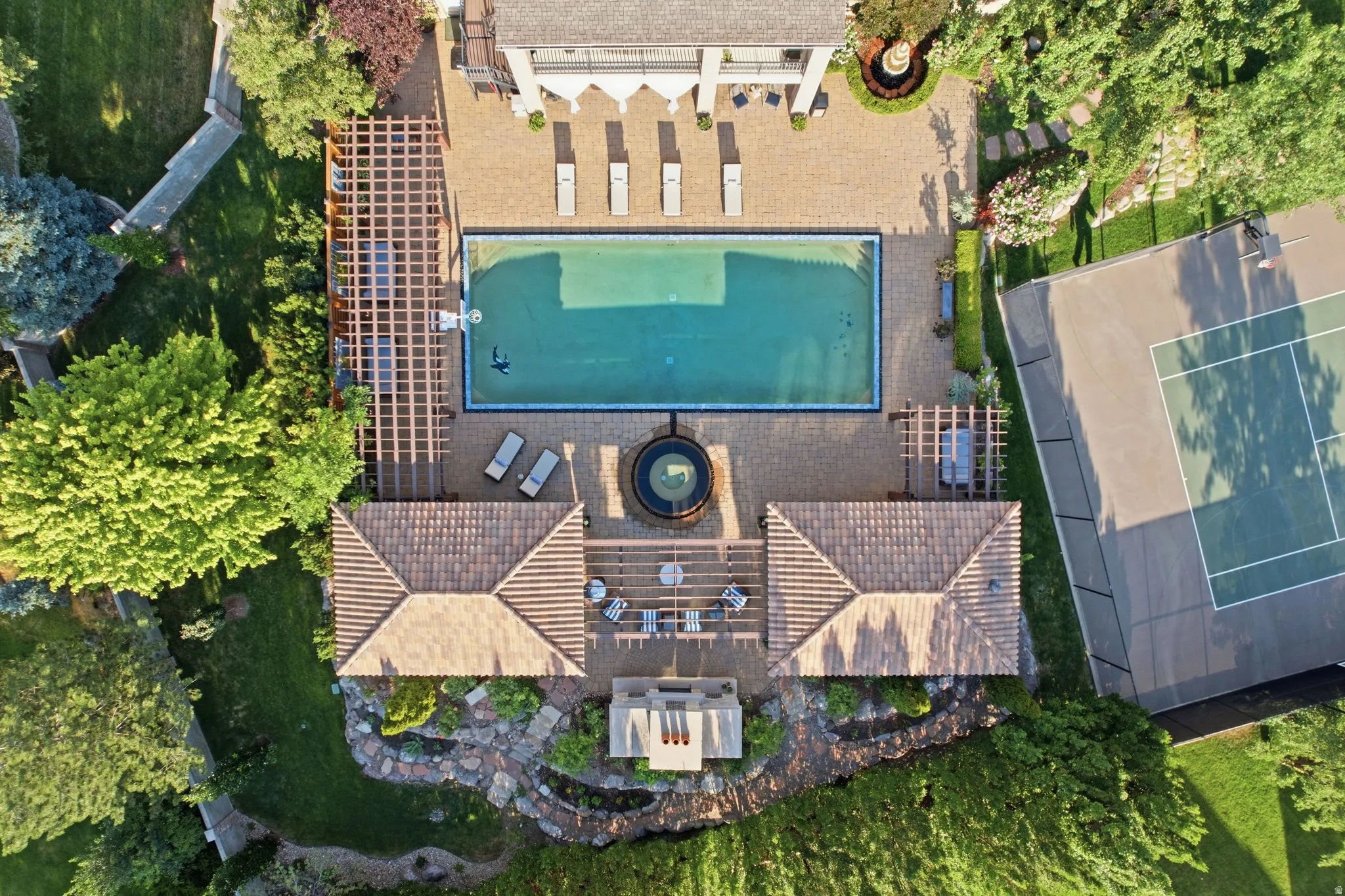 Expansive outdoor space featuring a rectangular swimming pool, integrated spa, full-size tennis court, and multiple pergolas