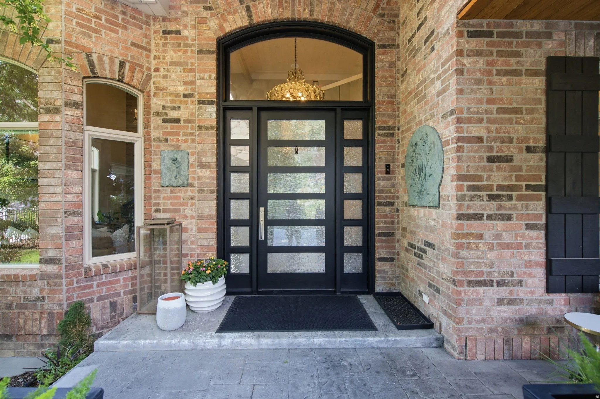 Brick exterior with arched detailing, black framed multi-pane entry door, transom window, and stone-finish porch