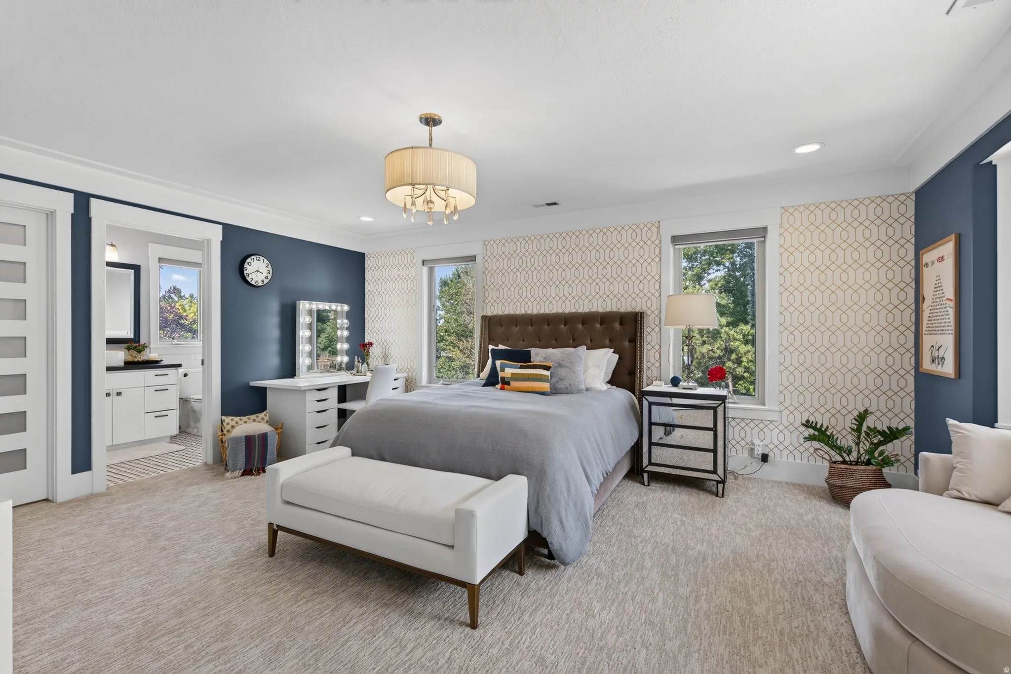 Recessed lighting with a central chandelier, patterned accent wall, and a full en-suite bathroom with a vanity and mirror