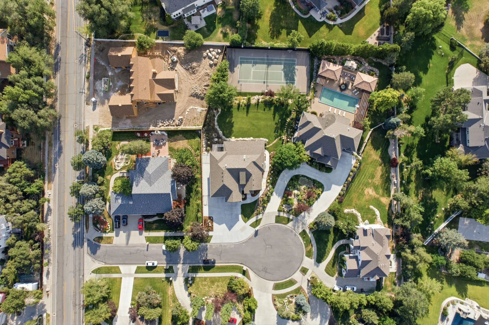 Aerial view highlighting residential properties, mature trees, a cul-de-sac, paved driveways, and a swimming pool with an adjacent tennis court
