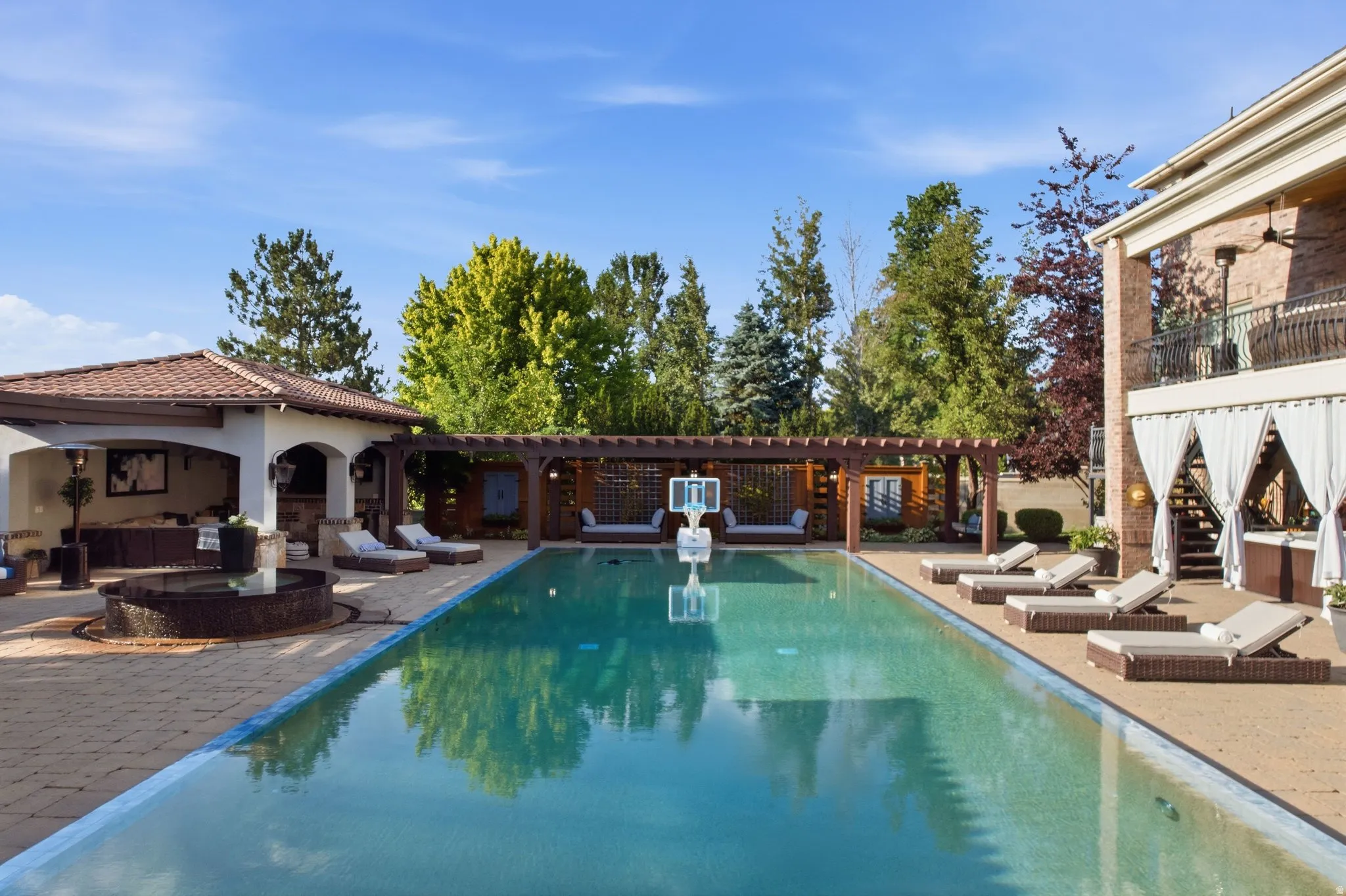 Expansive outdoor swimming pool with surrounding paver patio, separate covered cabana, and a wood pergola