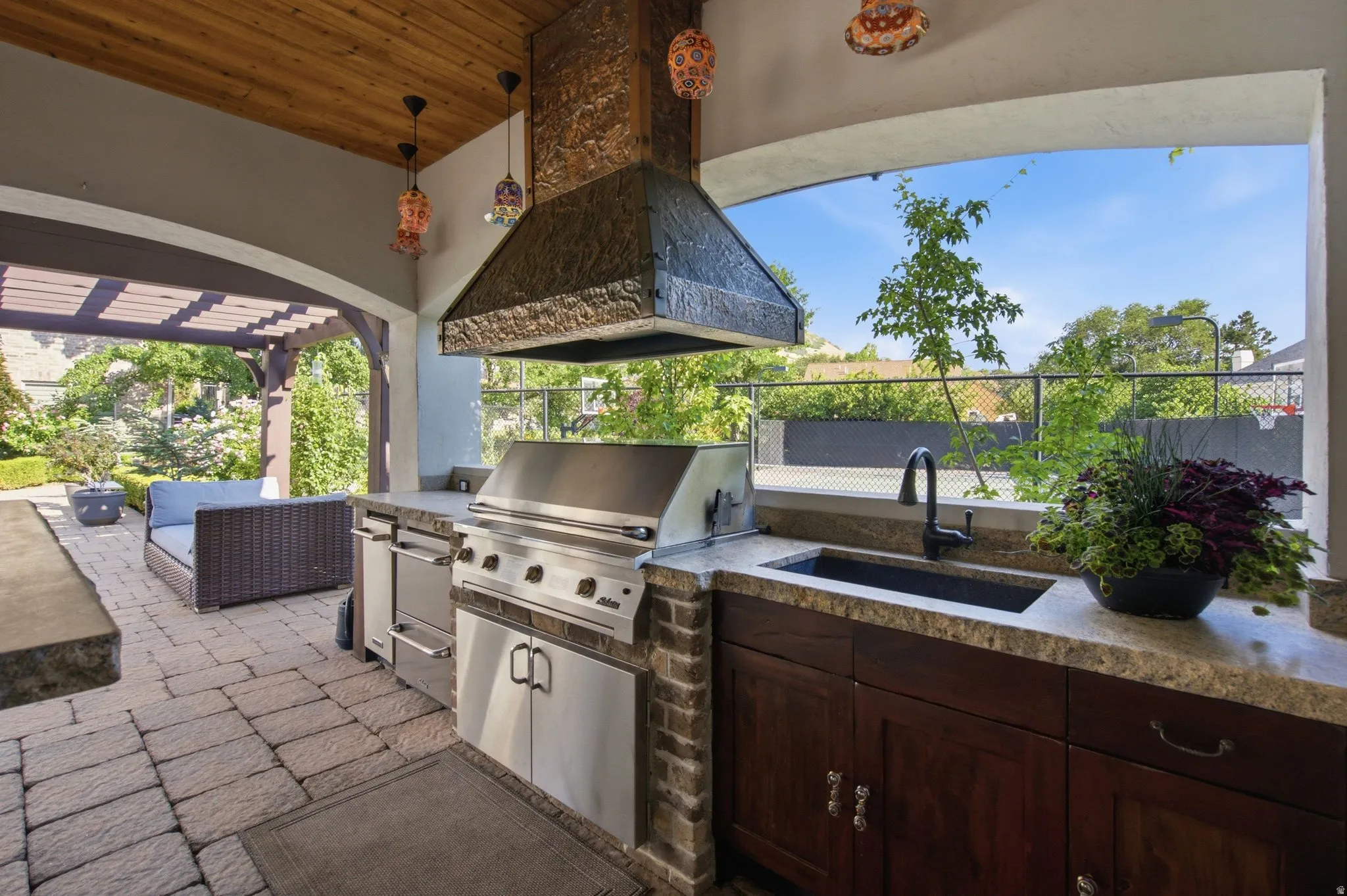 Outdoor kitchen with stone paver patio, wood plank ceiling, built-in grill, and dark wood cabinetry