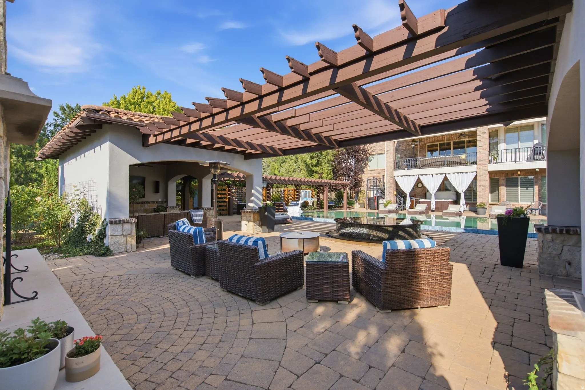 Expansive paver patio with a wood pergola, outdoor kitchen, and pool with an integrated spa
