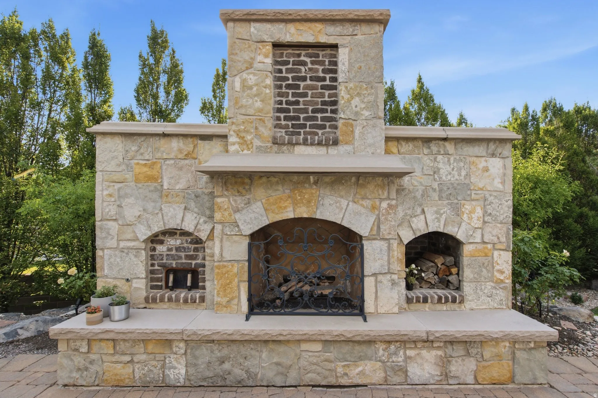 Stone-clad outdoor fireplace with hearth, arched firebox, and integrated wood storage