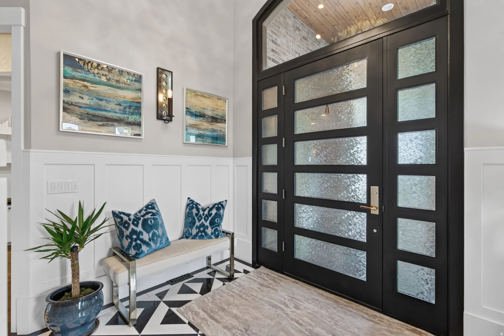Grand entry featuring a black multi-paneled door with frosted glass and transom window, wainscoting, and patterned tile flooring