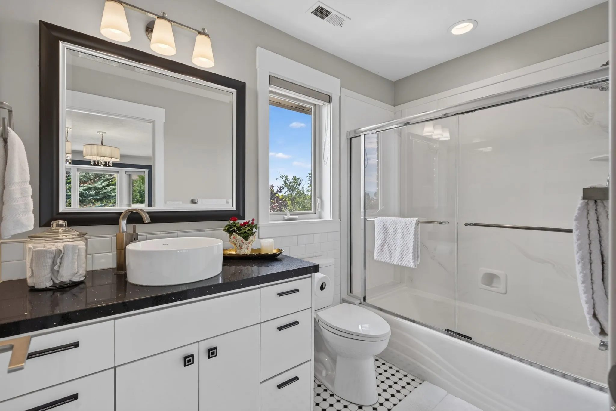 White vanity with dark countertop, vessel sink, and large framed mirror