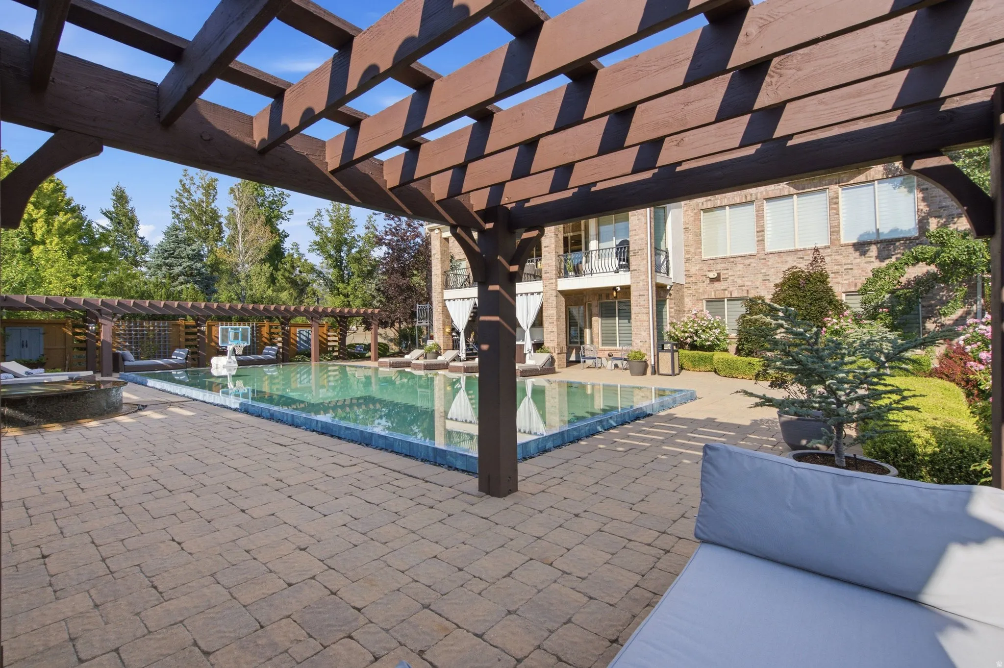 Expansive paver patio with a swimming pool, multiple pergolas, and a brick exterior residence