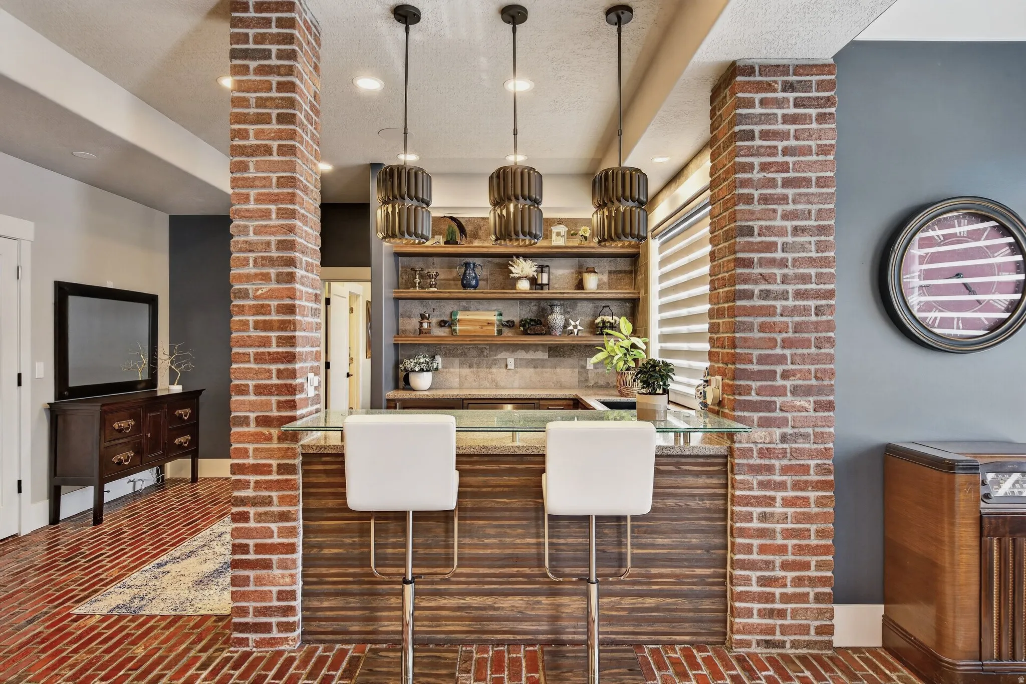 Exposed brick columns and flooring, custom built-in shelving, wood-finish bar paneling, and three pendant light fixtures