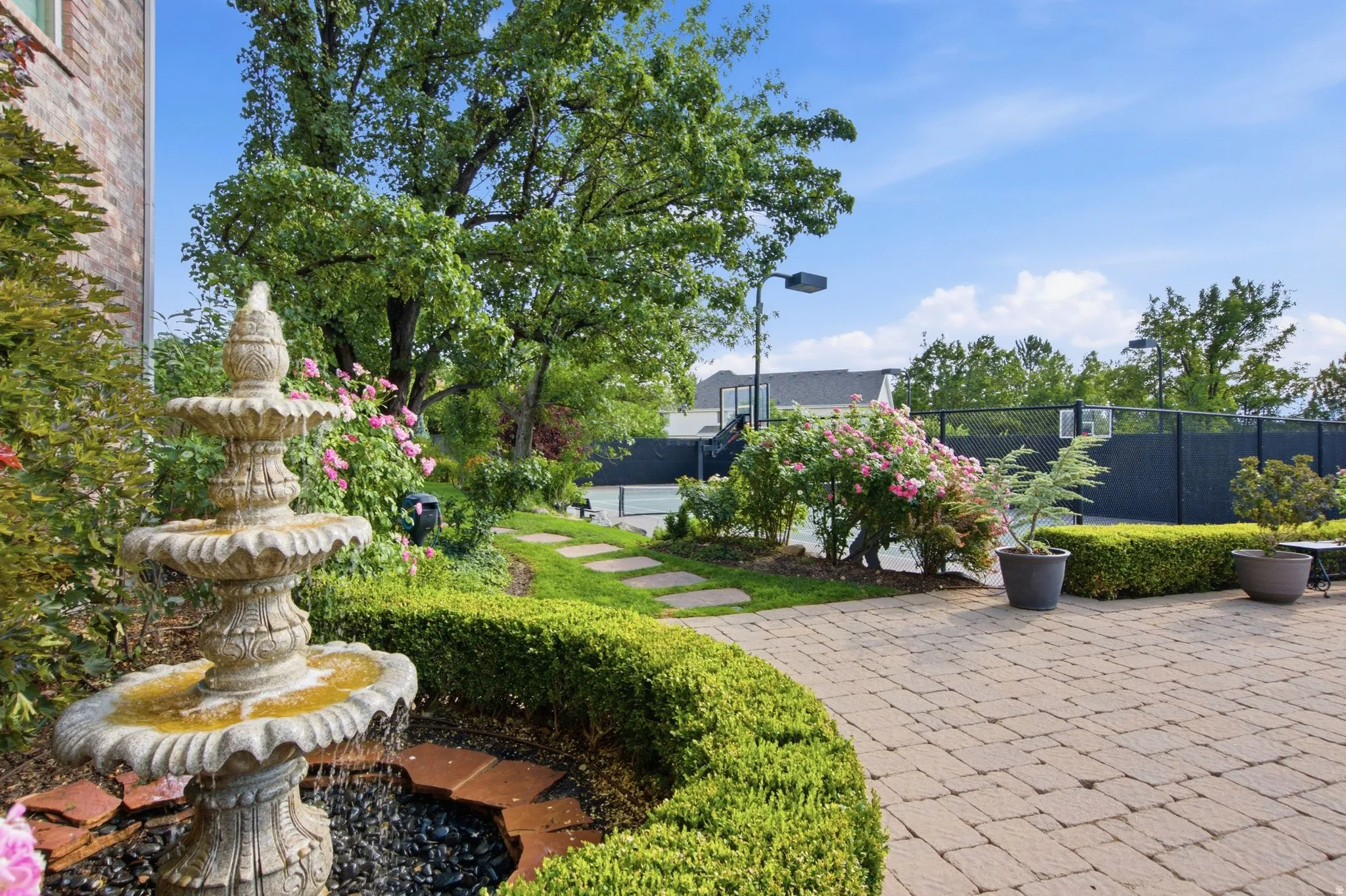 Paved patio with a tiered stone fountain, surrounded by manicured landscaping and a stone pathway