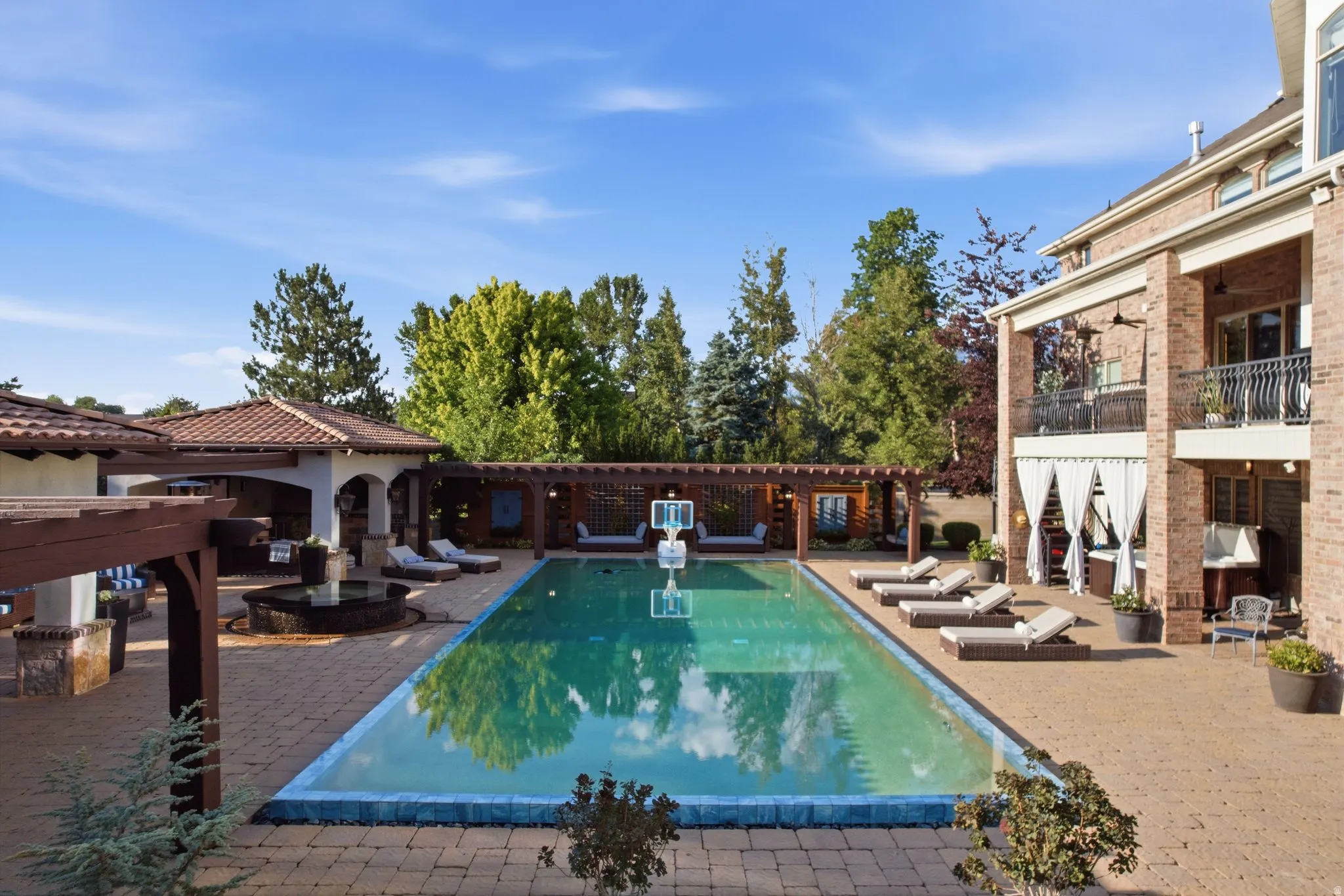 Expansive outdoor living area featuring a rectangular swimming pool, brick paver patio, and multiple pergolas