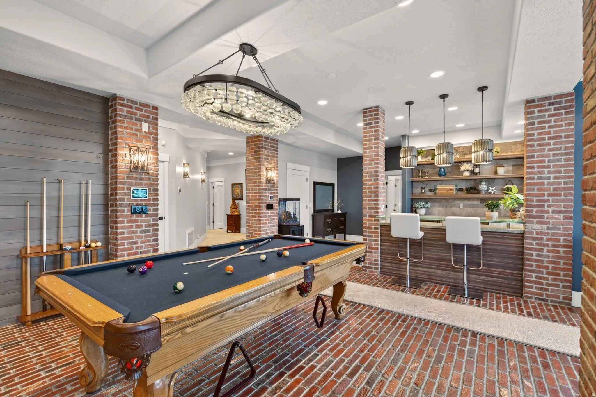 Exposed brick columns and flooring, shiplap accent wall, built-in wet bar with open shelving, and a decorative chandelier