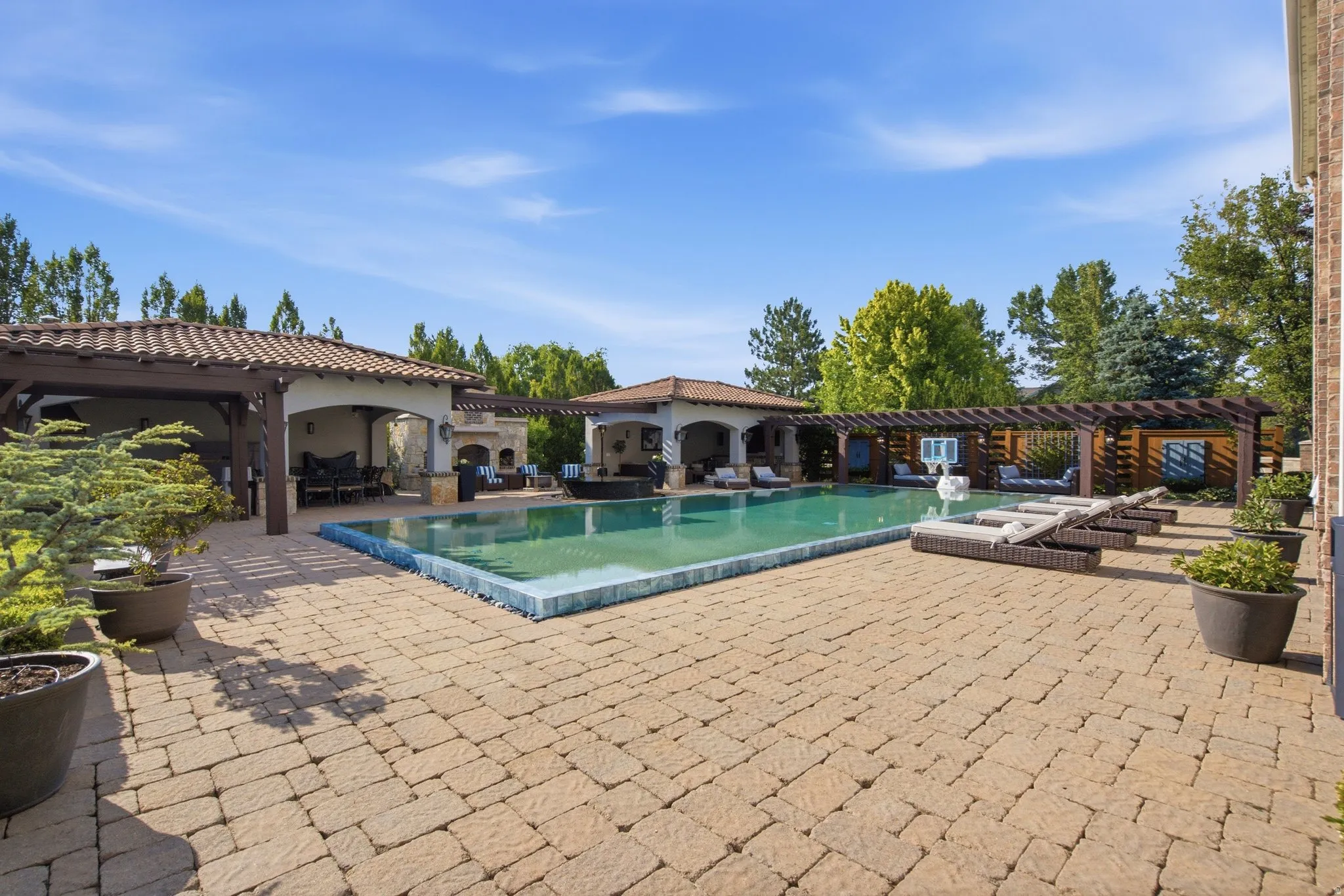 Expansive paver patio featuring a swimming pool, multiple covered outdoor spaces, and a pergola-covered lounge area