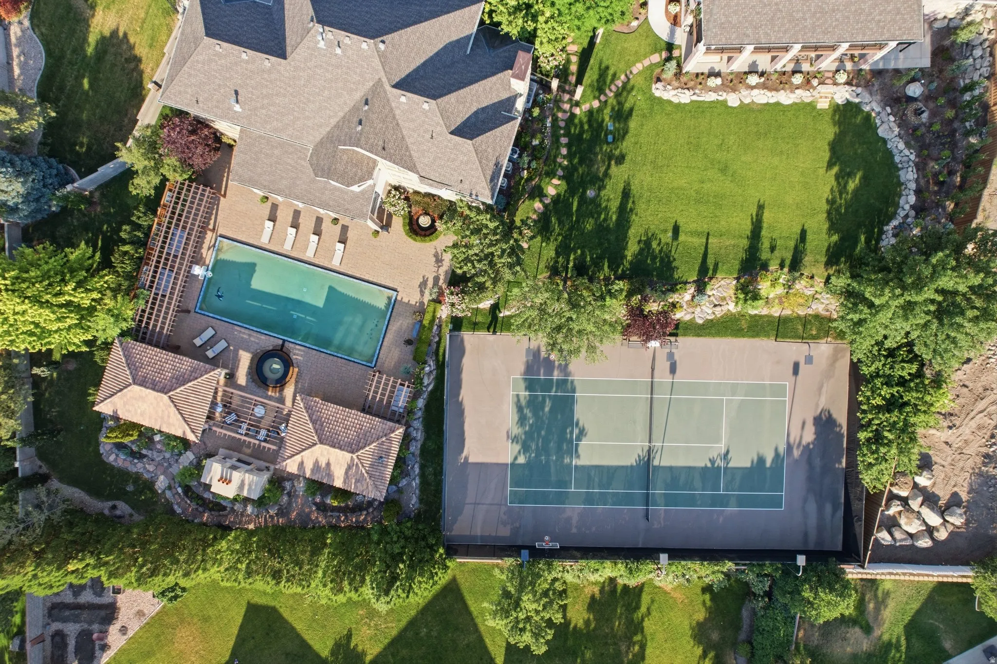 Outdoor swimming pool with integrated spa, expansive paver patio, tennis court, and manicured lawn