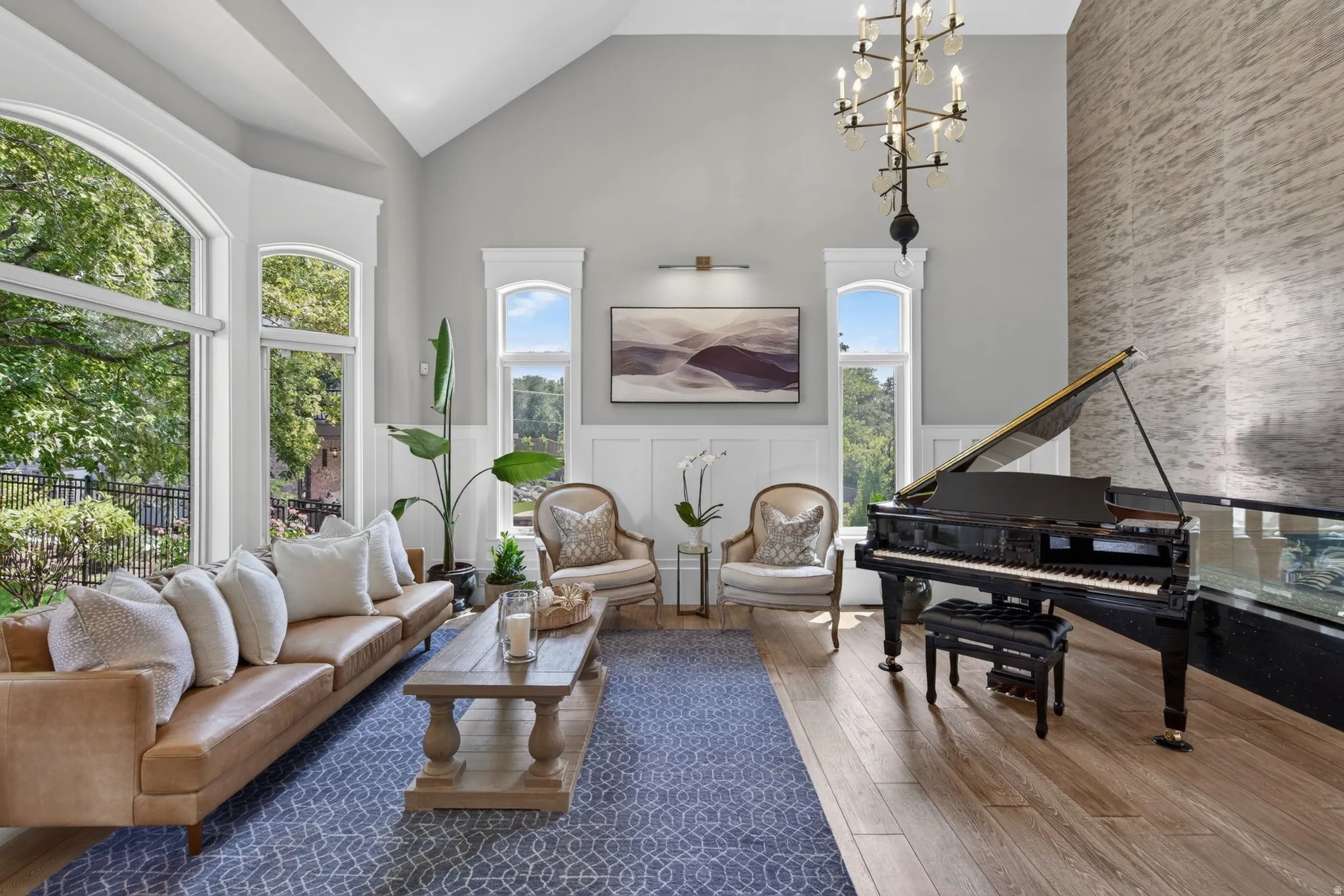 Vaulted ceiling with an ornate chandelier, expansive bay windows, wood-finish flooring, wainscoting, and a textured accent wall