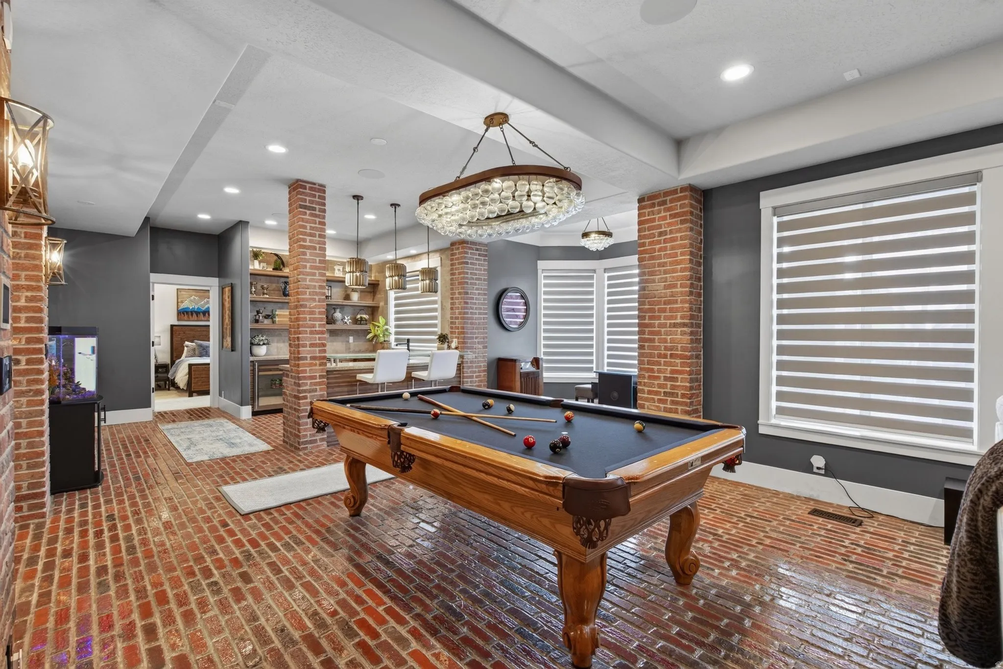 Brick-finish flooring, exposed brick pillars, built-in shelving, chandelier lighting, and a built-in wet bar
