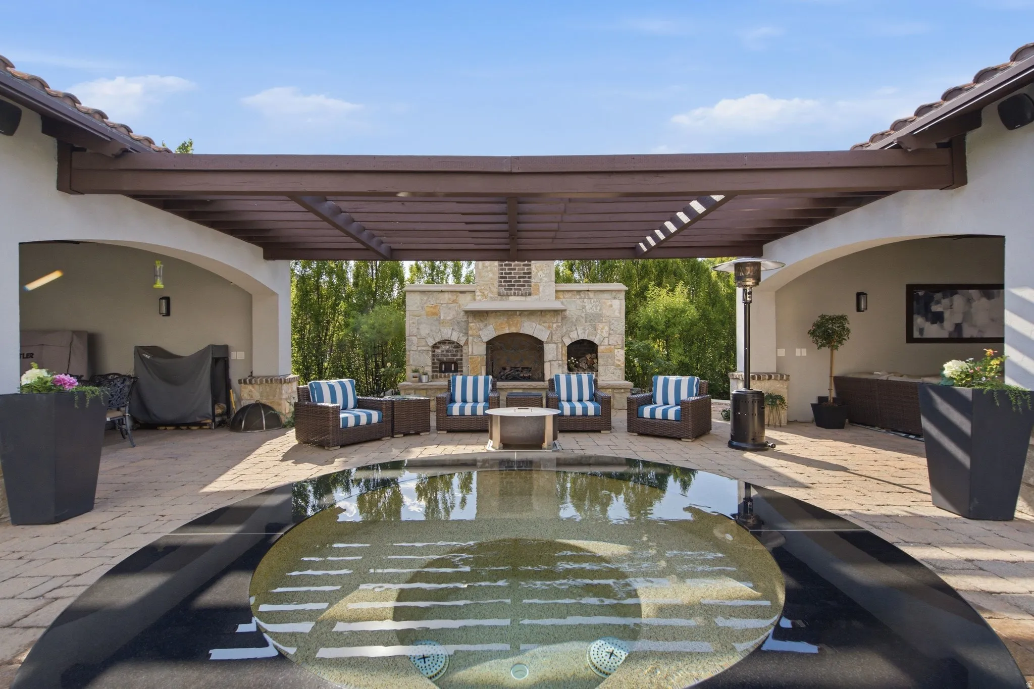 Outdoor living area featuring a central water feature, stone fireplace, and an overhead pergola