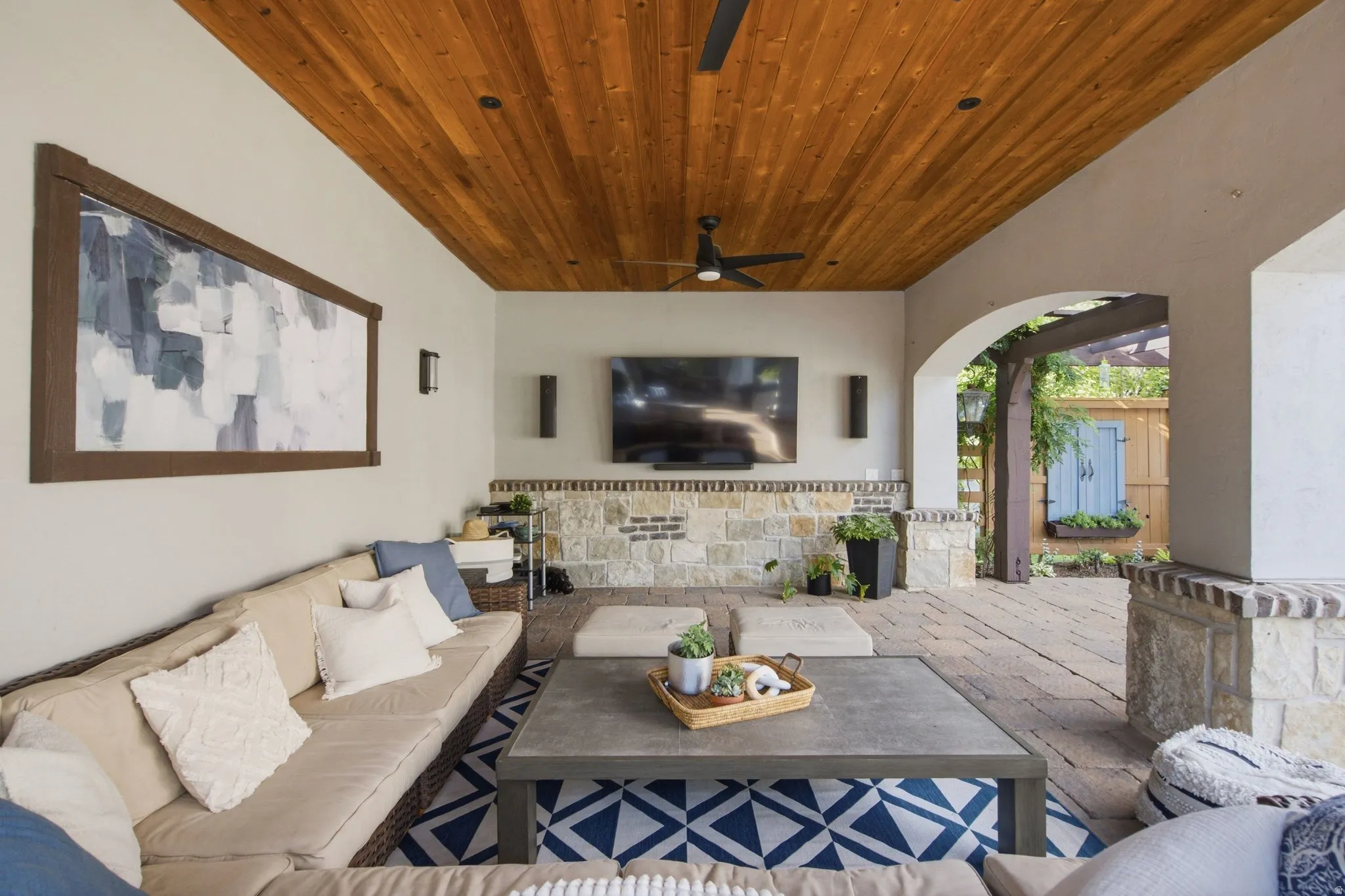 Outdoor living area featuring a wood-paneled ceiling, stone accent wall, ceiling fan, and arched entryway