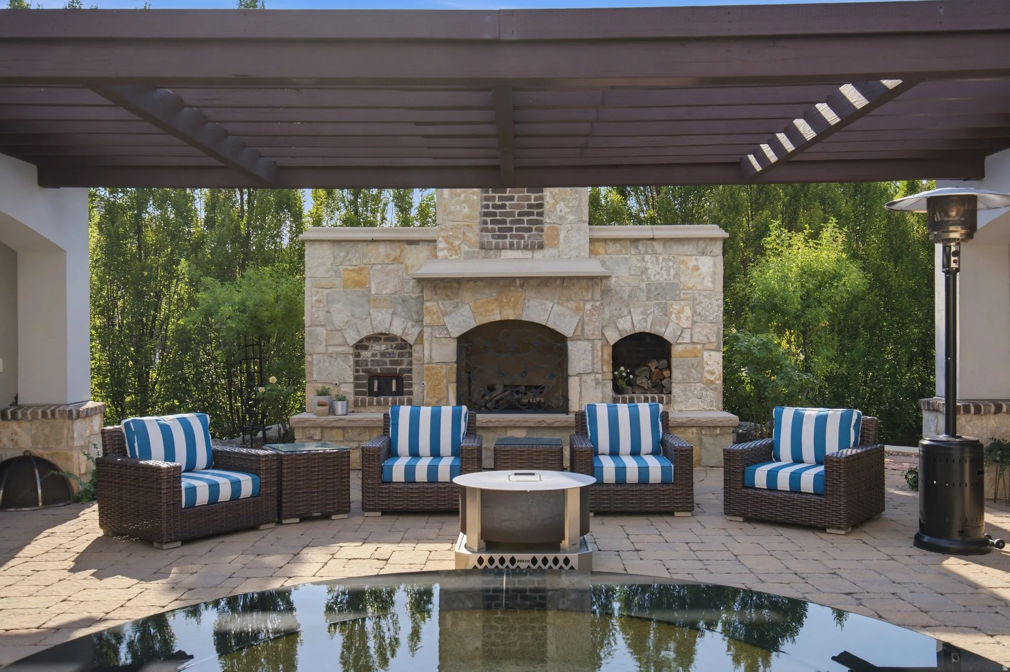 Covered outdoor patio featuring a stone fireplace, brick accents, and a paved surface
