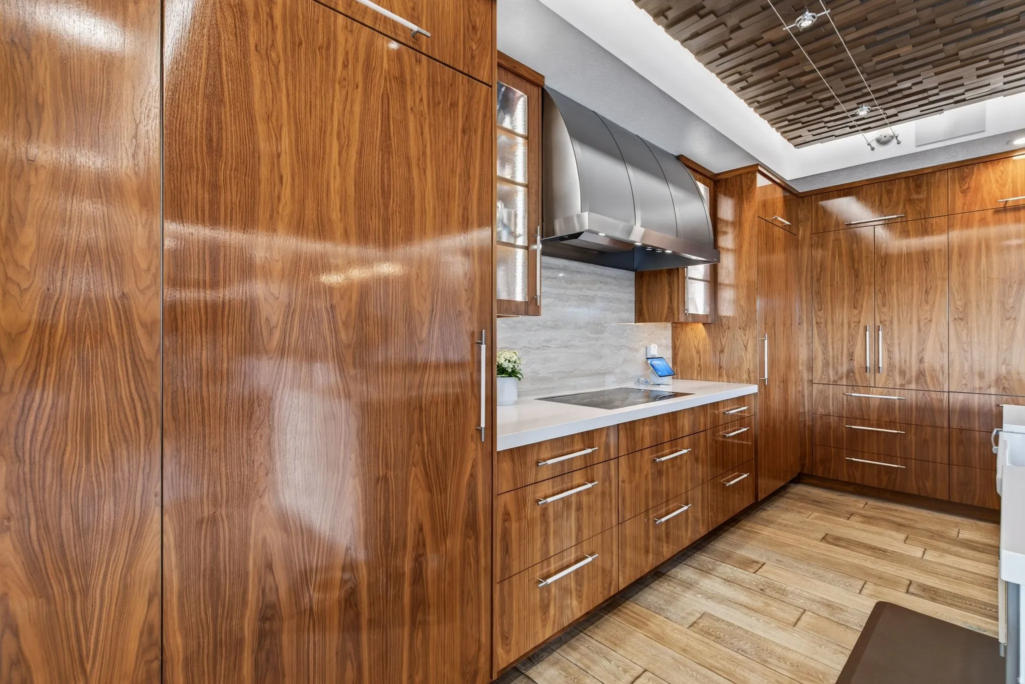 Custom wood-finish cabinetry, stainless steel range hood, built-in cooktop, light-toned countertop, and wood-finish flooring