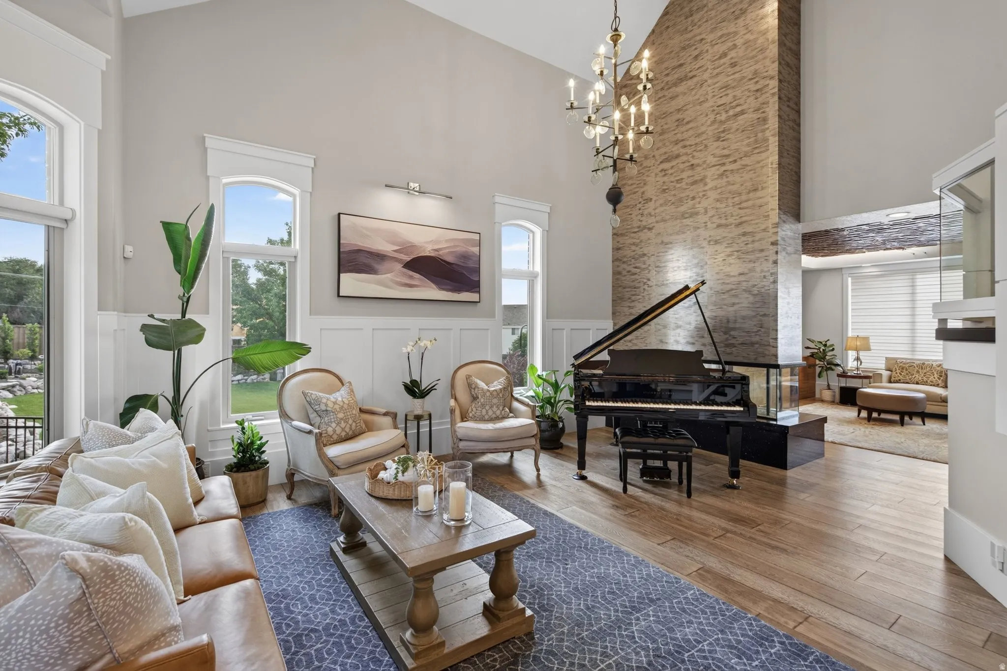 Two-story living area featuring wood-finish flooring, a stone-clad accent wall, a grand piano, and a contemporary chandelier