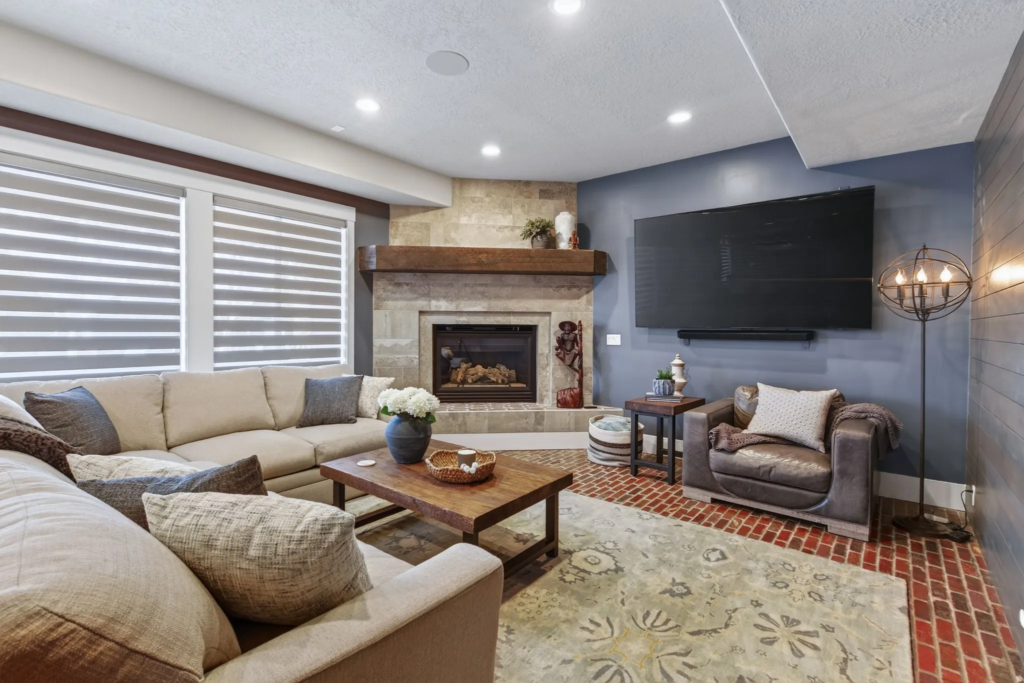 Stone-clad fireplace with a wood mantle, recessed lighting, and dual window treatments