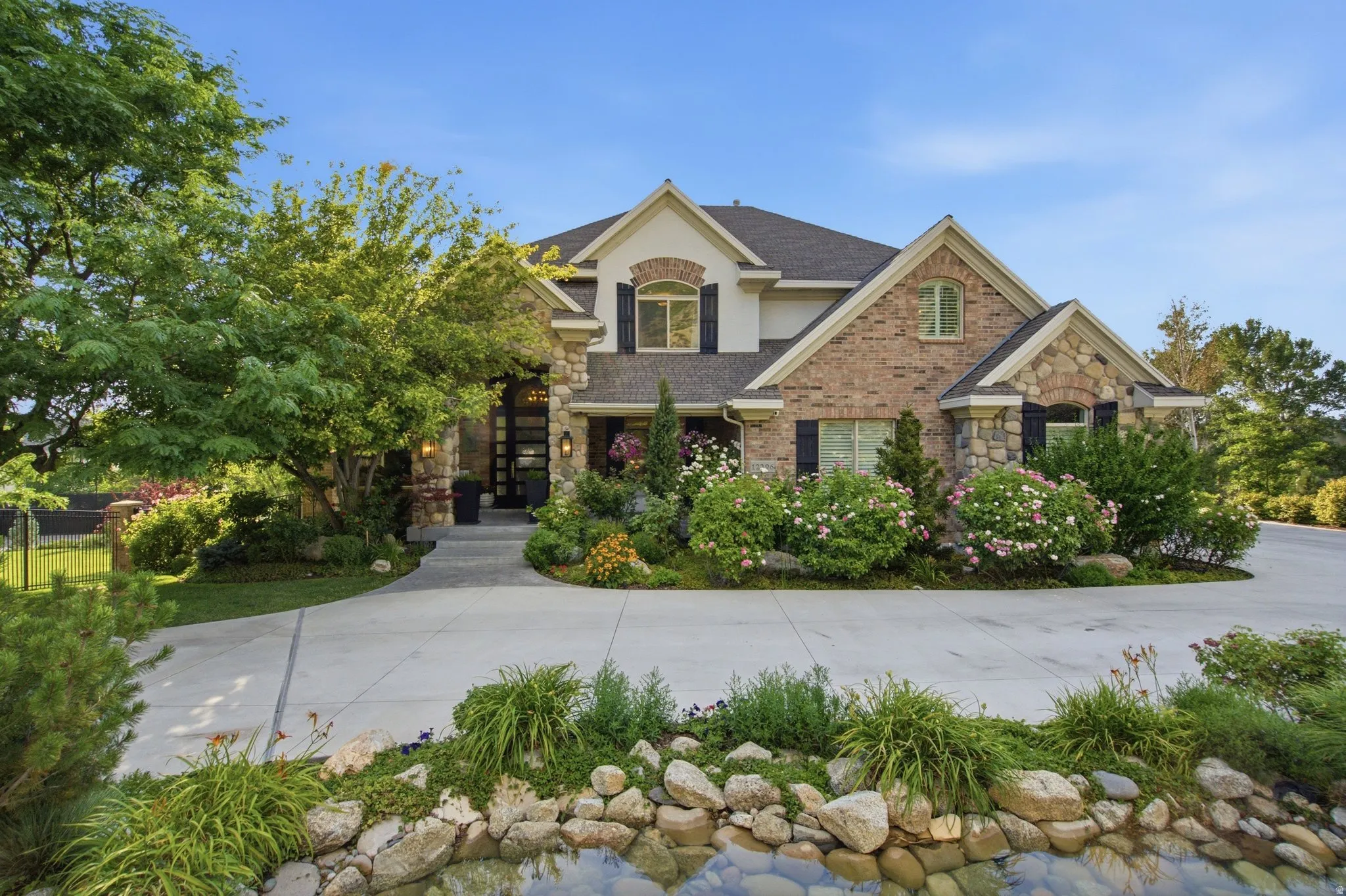 Stunning exterior featuring stone and brick accents, a gabled roofline, and mature landscaping