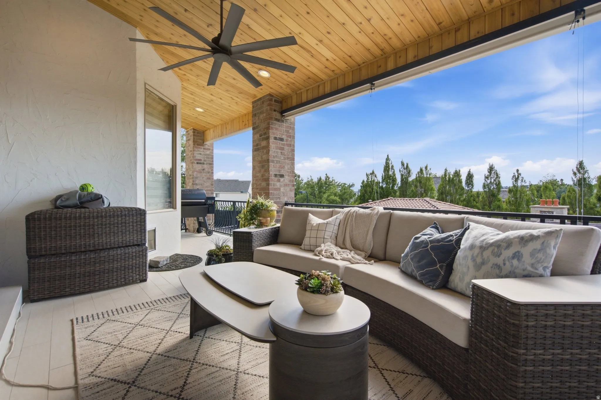 Expansive covered patio featuring a wood-panel ceiling, large ceiling fan, brick columns, and a railing