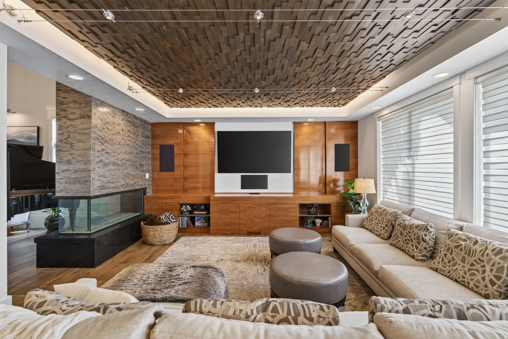 Textured wood ceiling, full-height stone-clad fireplace with integrated linear aquarium, wood-finish flooring, custom built-in media cabinetry, and recessed lighting