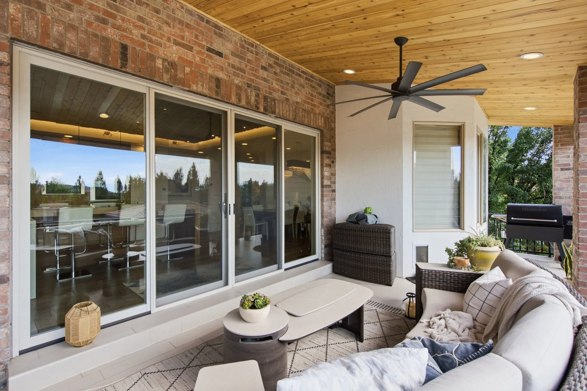Covered patio featuring a wood-finish ceiling, brick exterior wall, full-height sliding glass doors, and a ceiling fan