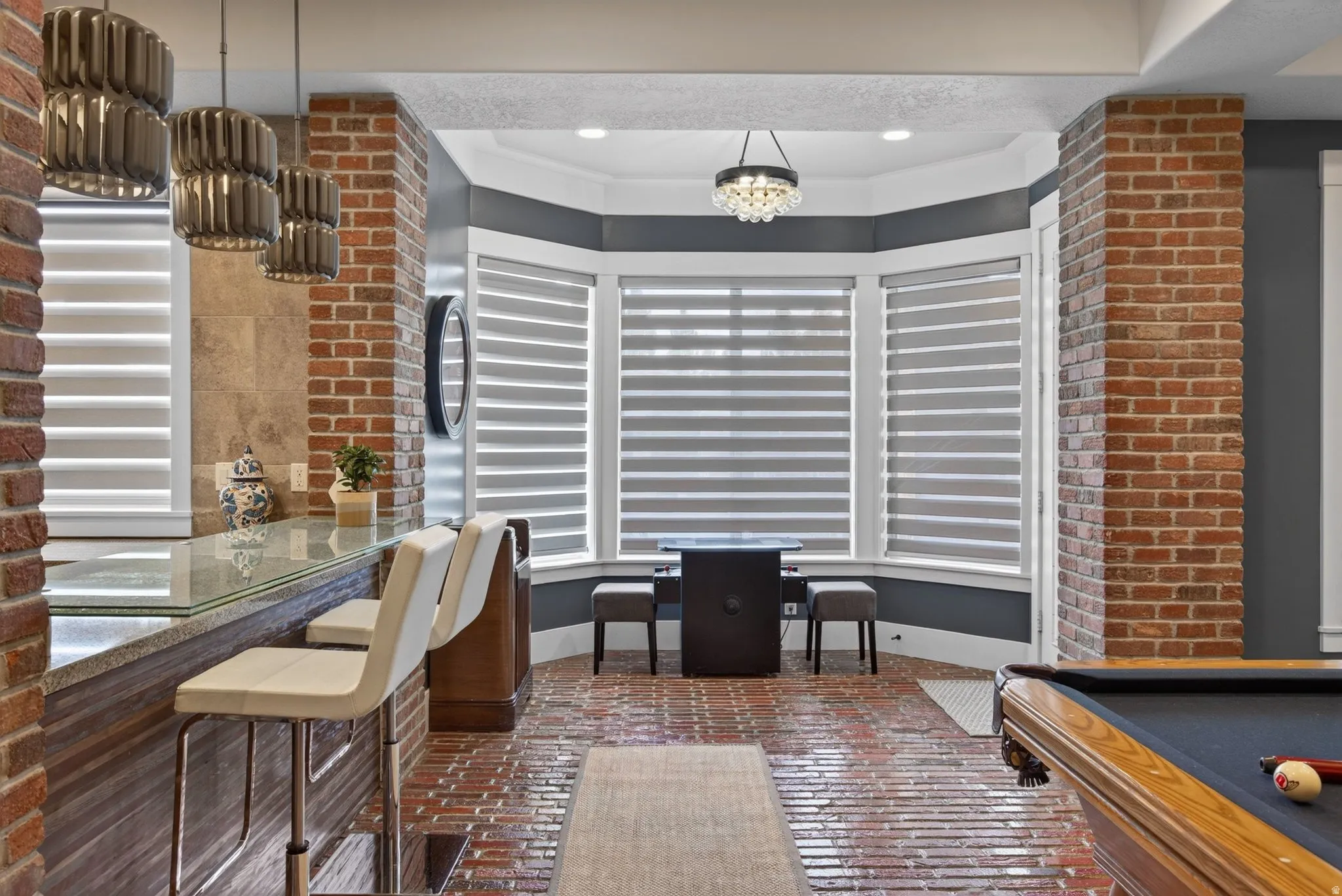 Brick-finish flooring with a bay window, recessed lighting, and a built-in bar featuring a polished countertop and pendant lighting