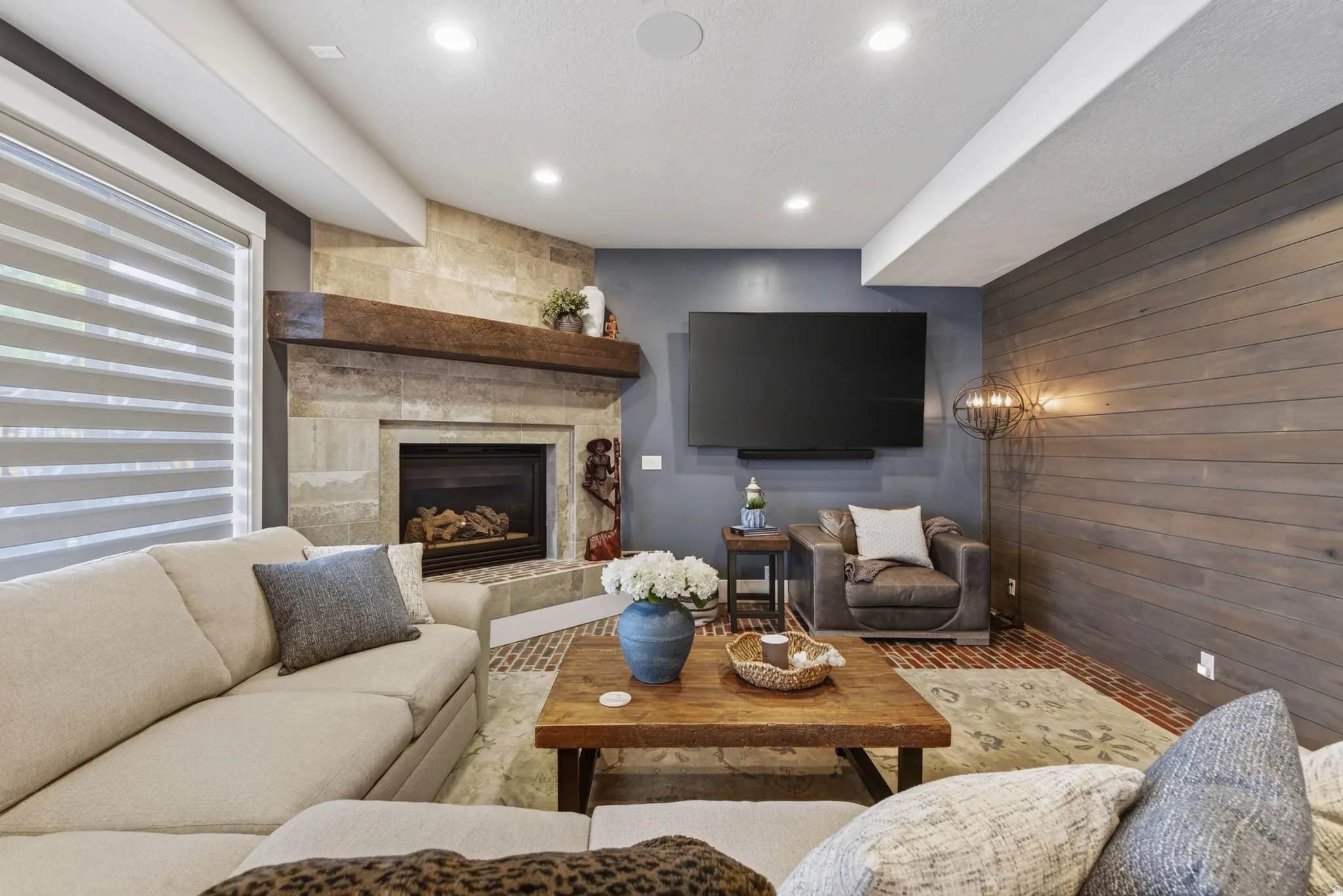 Built-in fireplace with a stone surround and wood mantle, shiplap accent wall, recessed lighting, and wood-finish flooring
