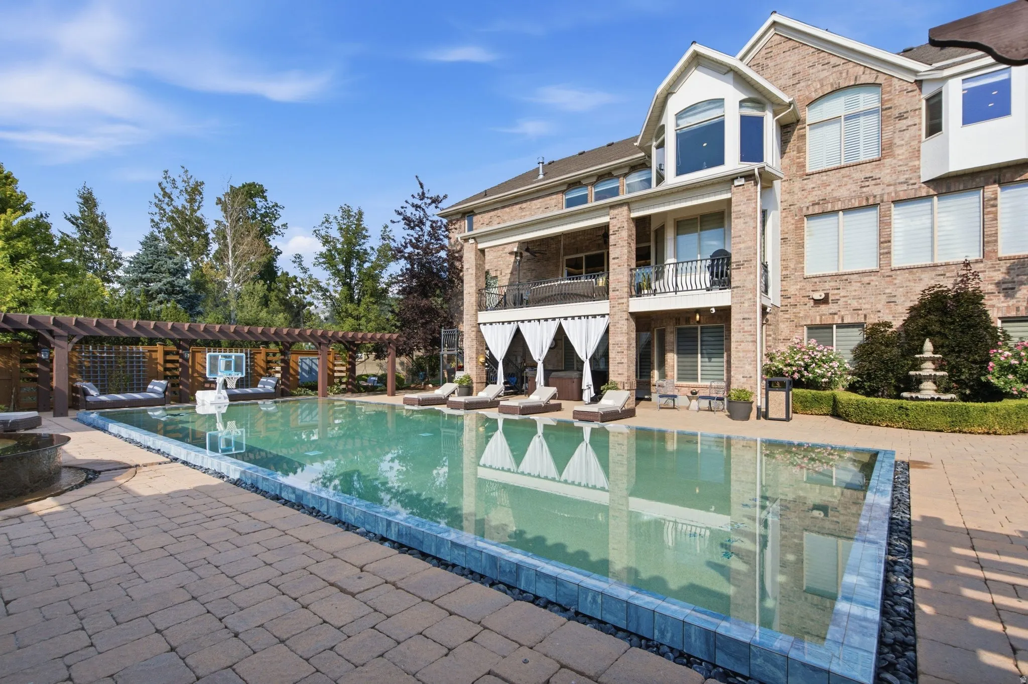 Expansive paver patio with a rectangular swimming pool, integrated pergola, and a tiered fountain