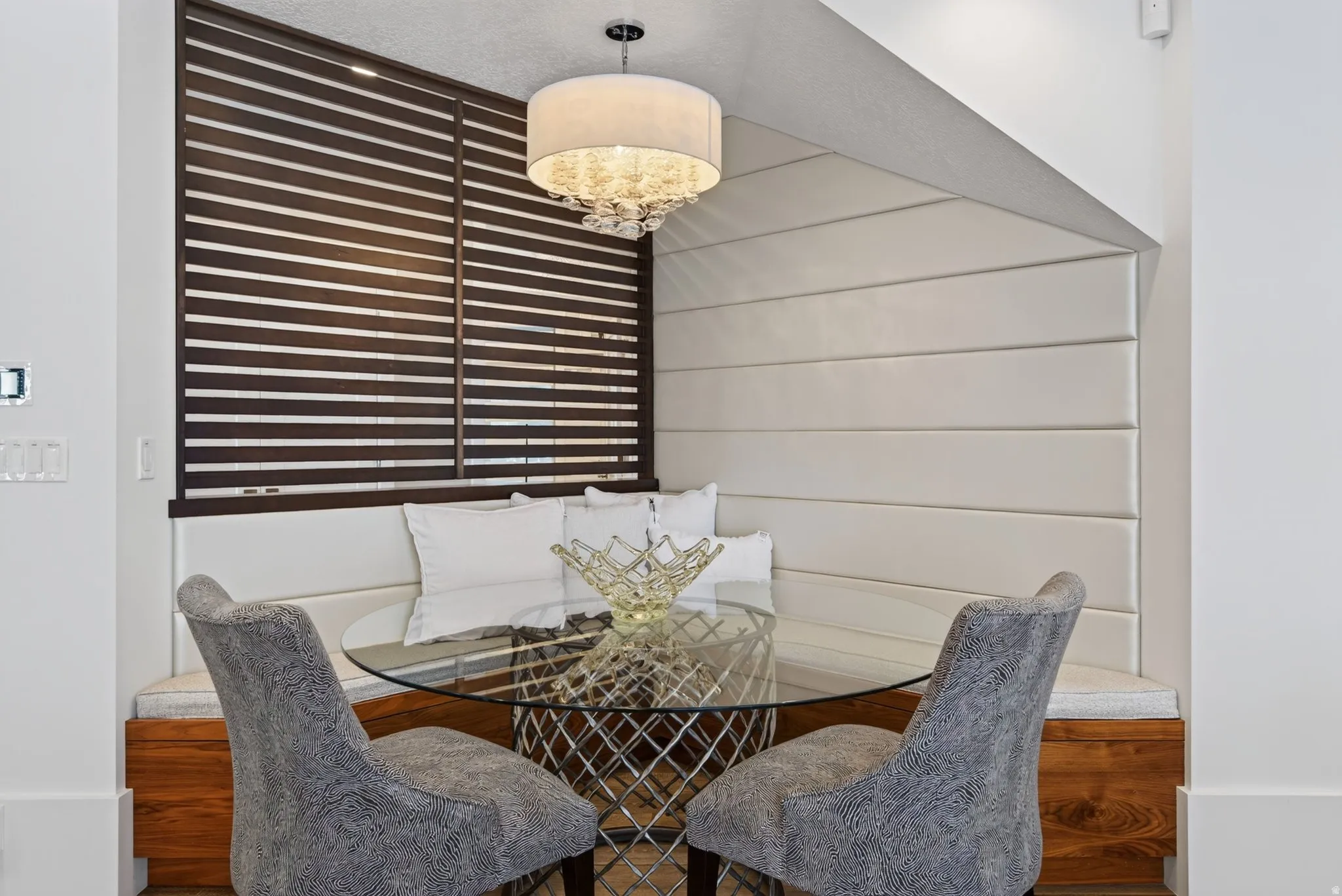 Built-in banquette seating with upholstered back paneling, wood-finish base, and a contemporary chandelier