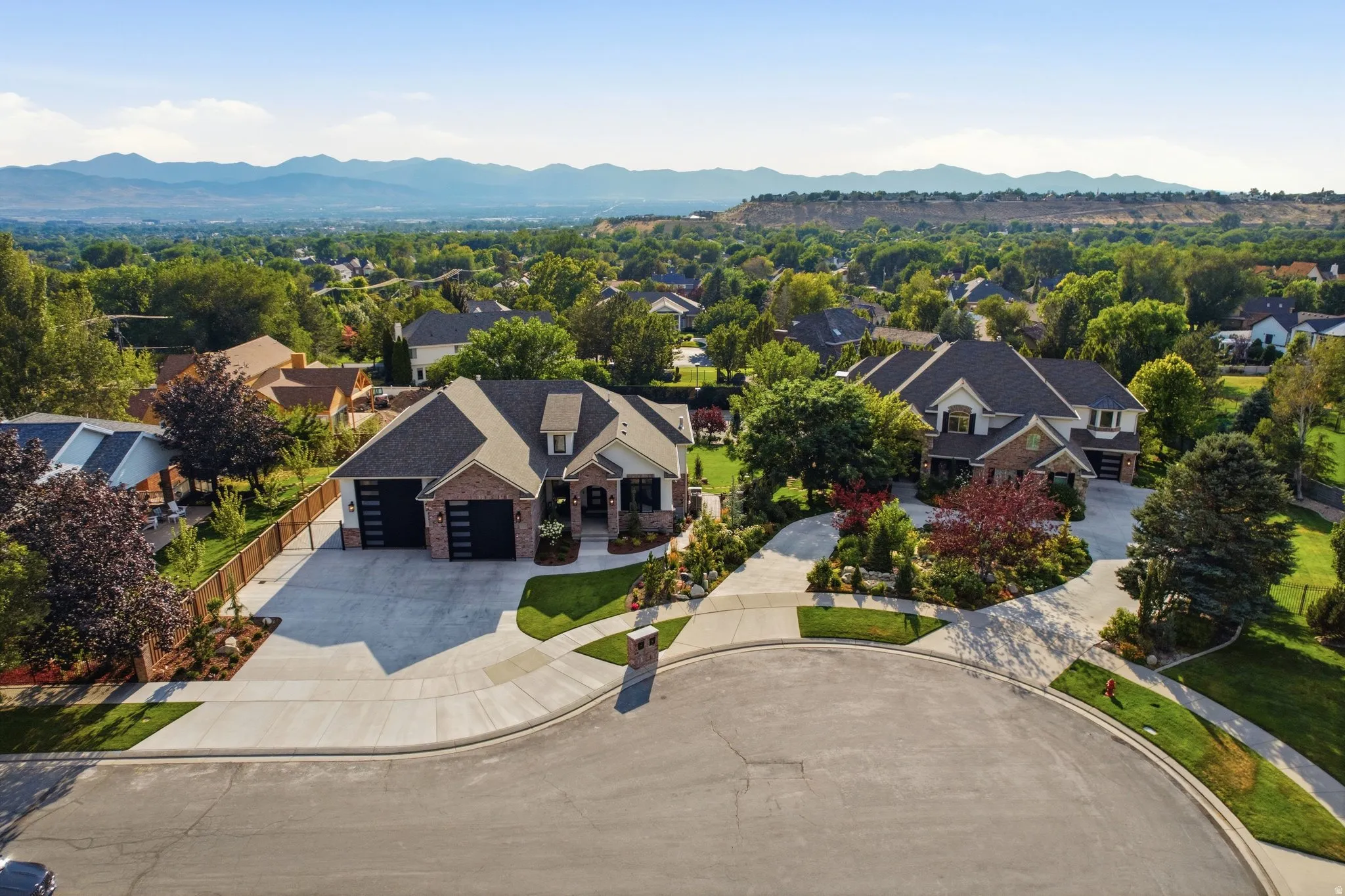Brick exterior with dark garage doors, concrete driveway, and mature landscaping