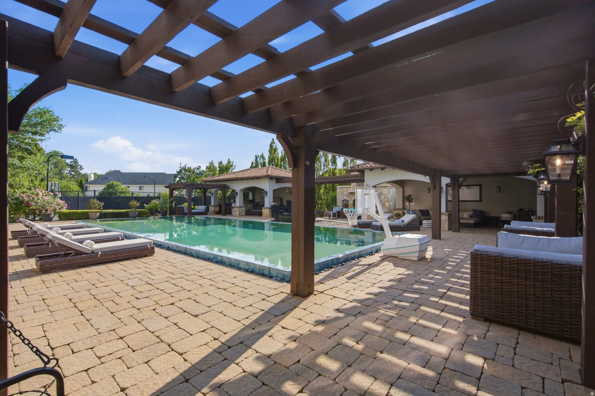 Expansive outdoor living area featuring a large swimming pool, paver patio, and dark wood pergola
