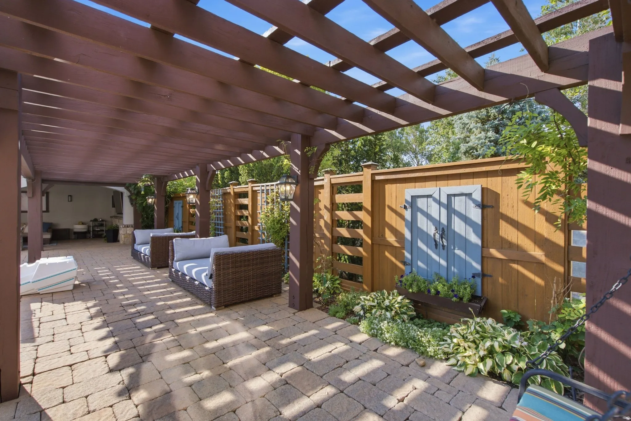 Expansive paver patio with a large wooden pergola, perimeter wood fencing, and integrated garden beds