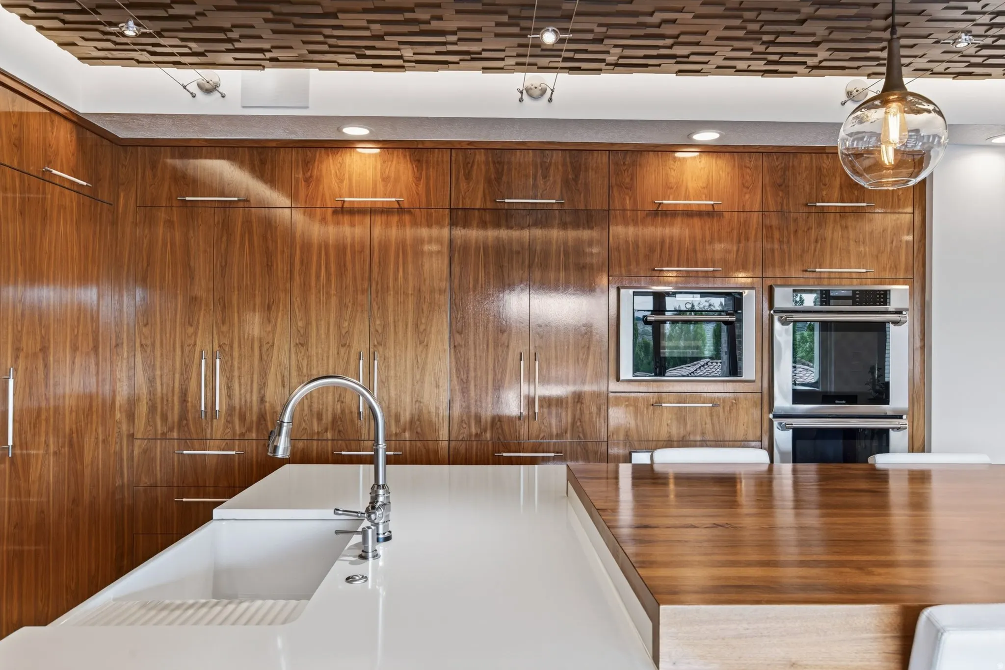 Integrated stainless steel appliances, wood-finish cabinetry, white solid surface countertop with integrated sink, and wood-finish island countertop