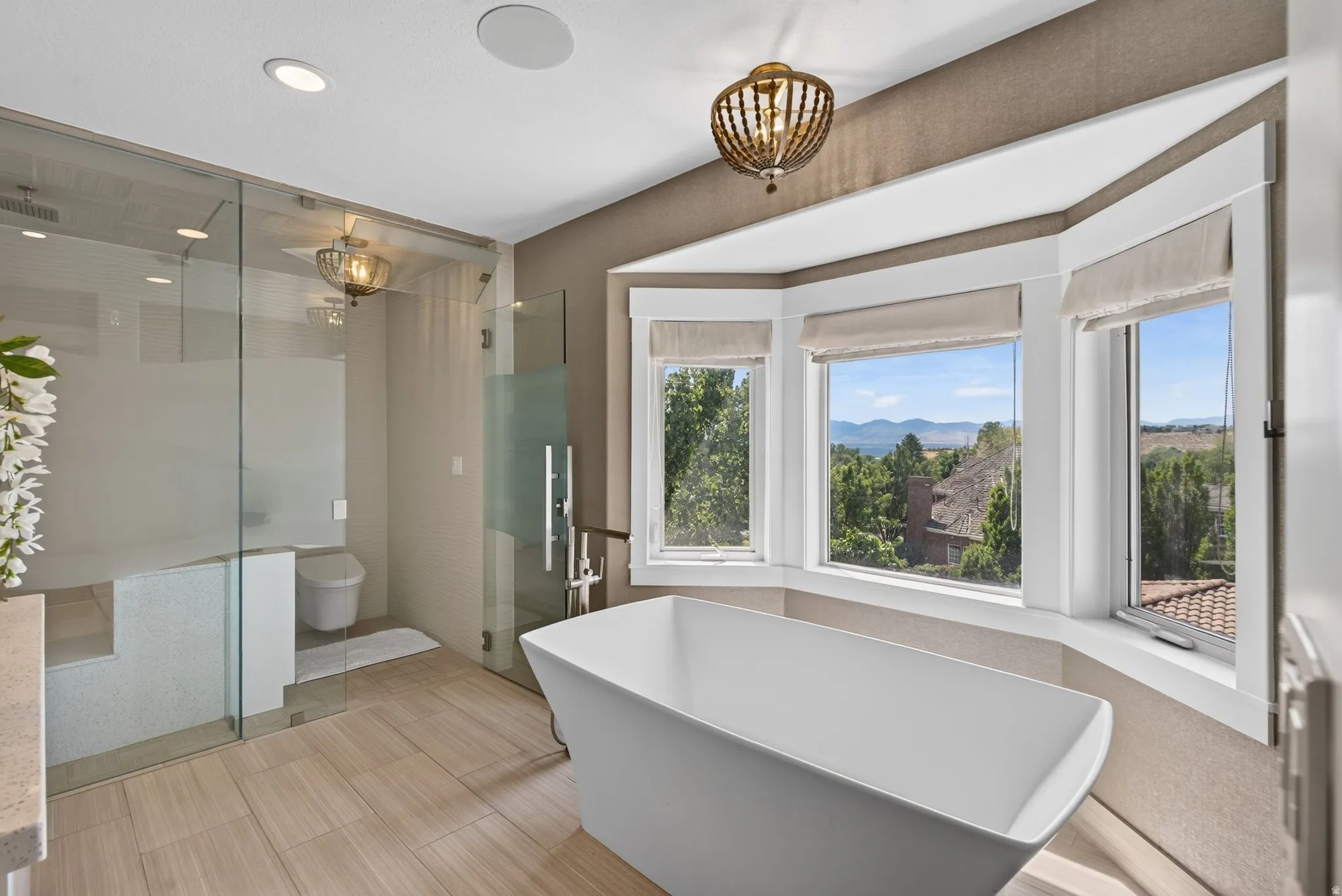Freestanding soaking tub, frameless glass shower enclosure, wood-look plank flooring, and a multi-window bay with distant scenery