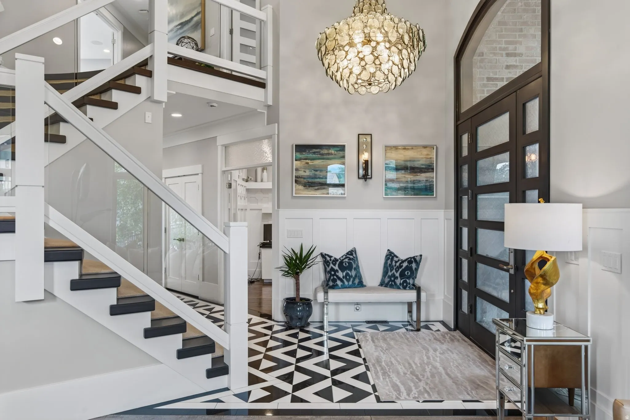 Grand entry featuring a modern chandelier, dark-framed glass paneled door, and a staircase with glass panel railings