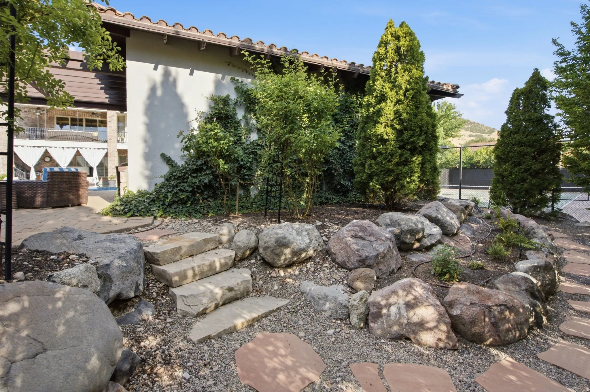 Terracotta roof tiles, stucco exterior, stone steps, and a landscaped rock garden