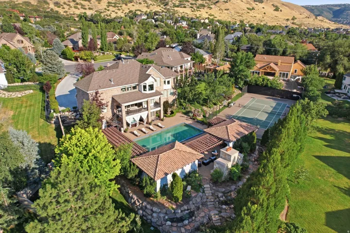 Expansive outdoor living area featuring a large swimming pool, a full-size tennis court, a covered patio, and a separate cabana with an outdoor fireplace